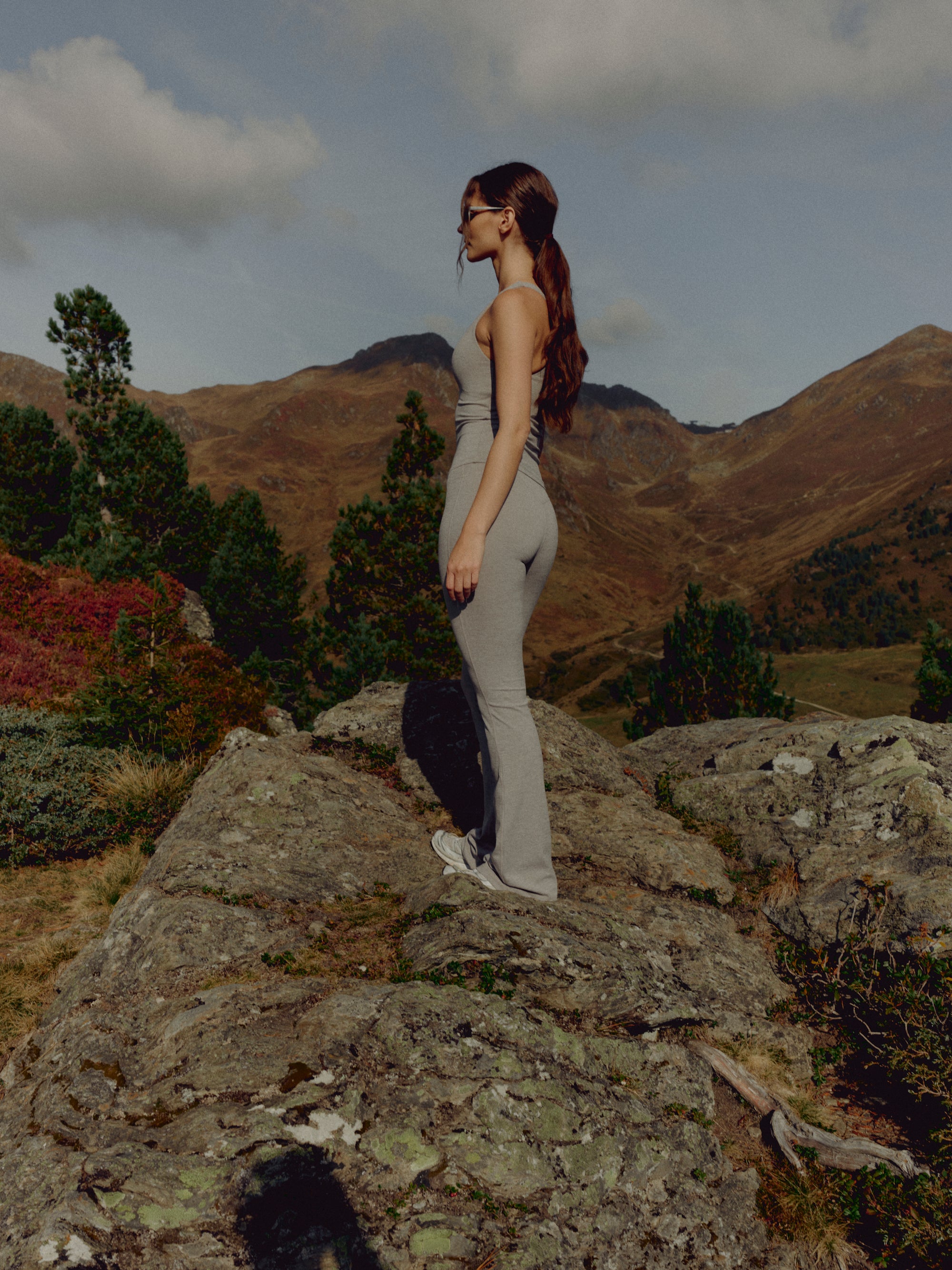 Woman wearing CASPARA Cloudform yoga pants in grey melange standing on a rocky mountain hillside.