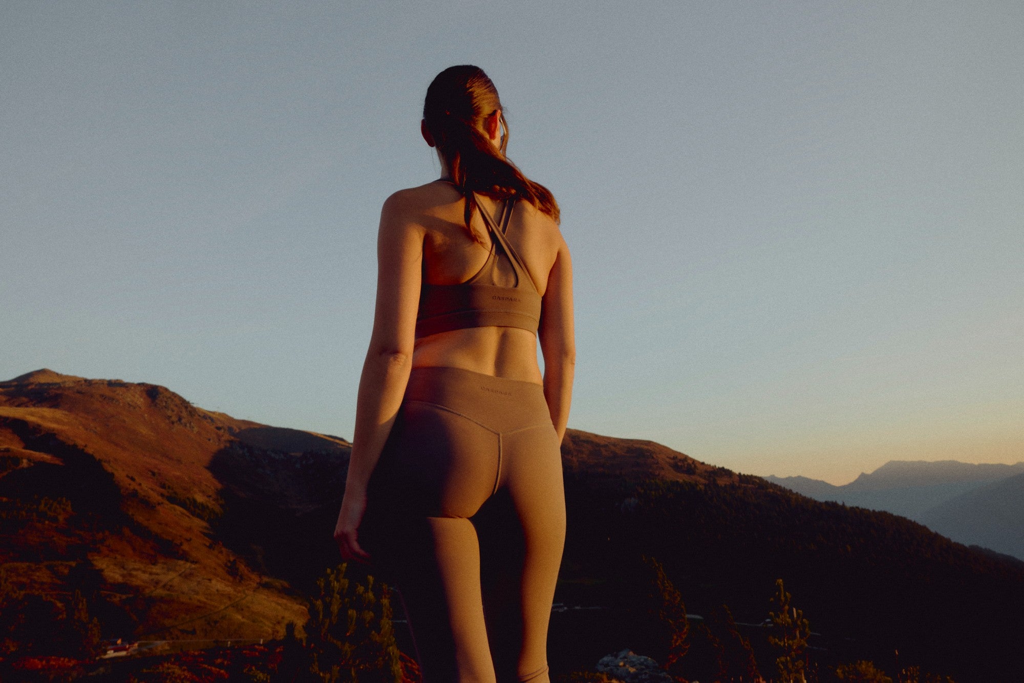 Woman wearing a walnut CASPARA Cloudform crossback sports bra overlooking mountains.