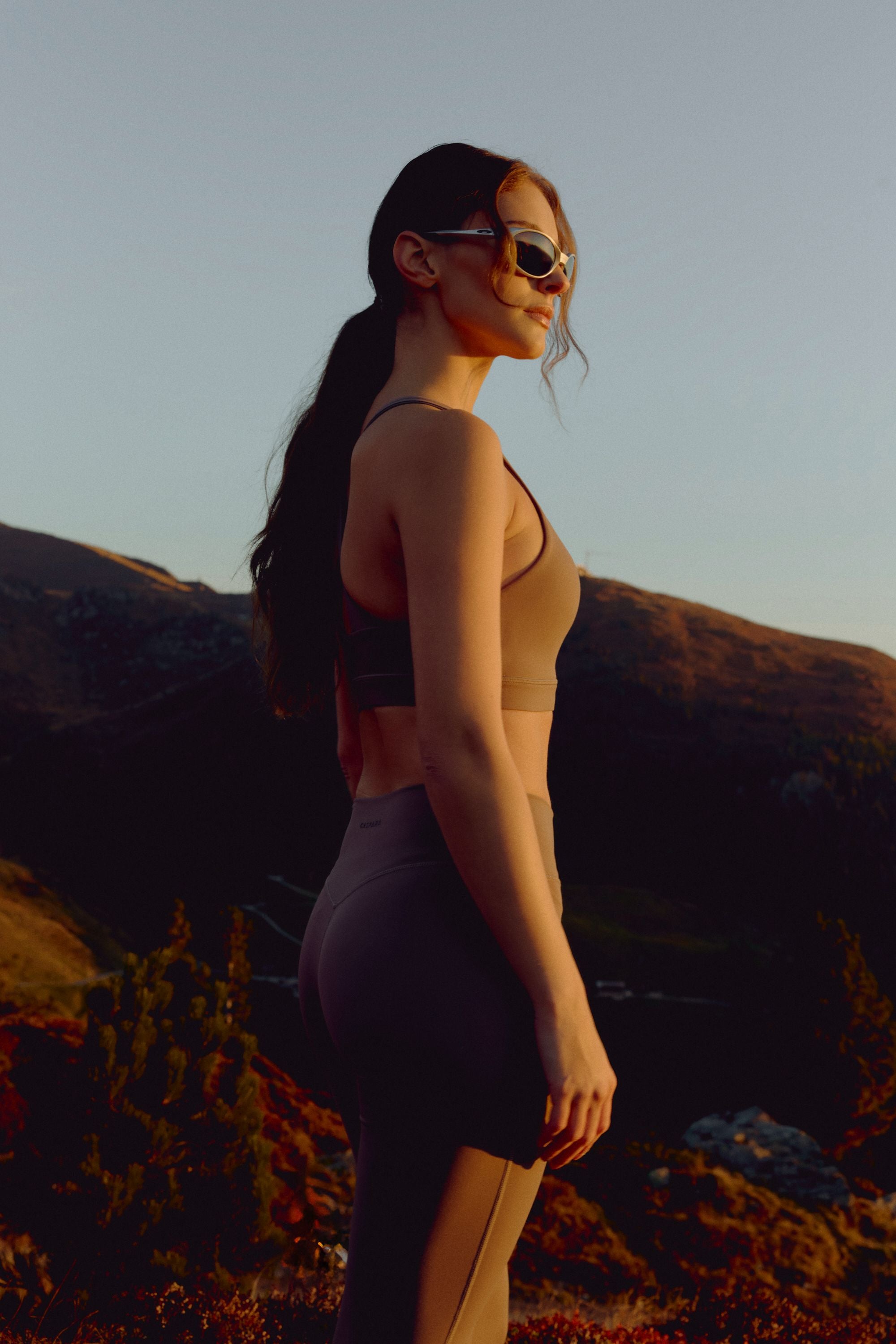 Woman wearing a walnut CASPARA Cloudform crossback sports bra in a mountain landscape.