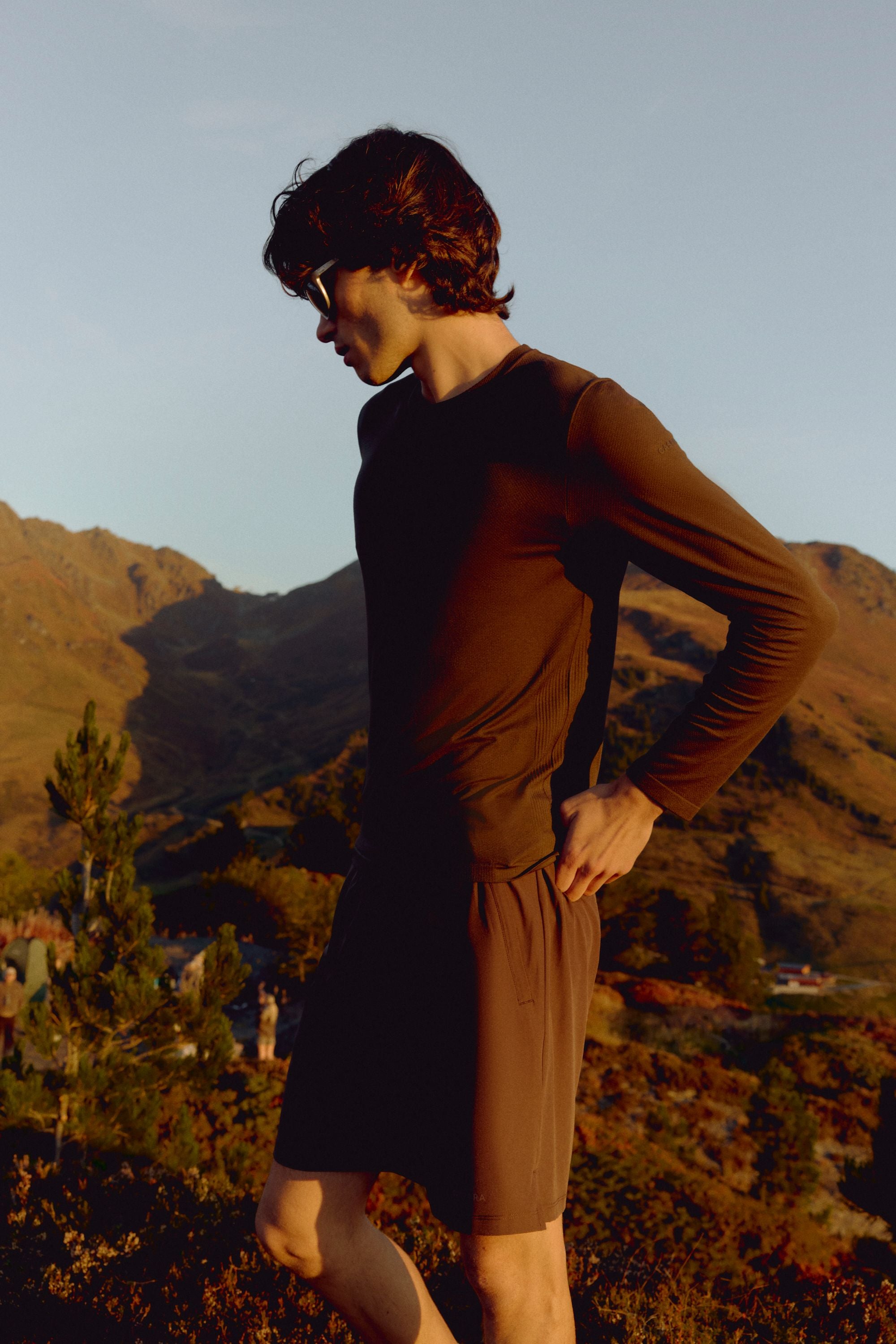 Man wearing an espresso CASPARA Seamlite long sleeve shirt on a mountain hillside.