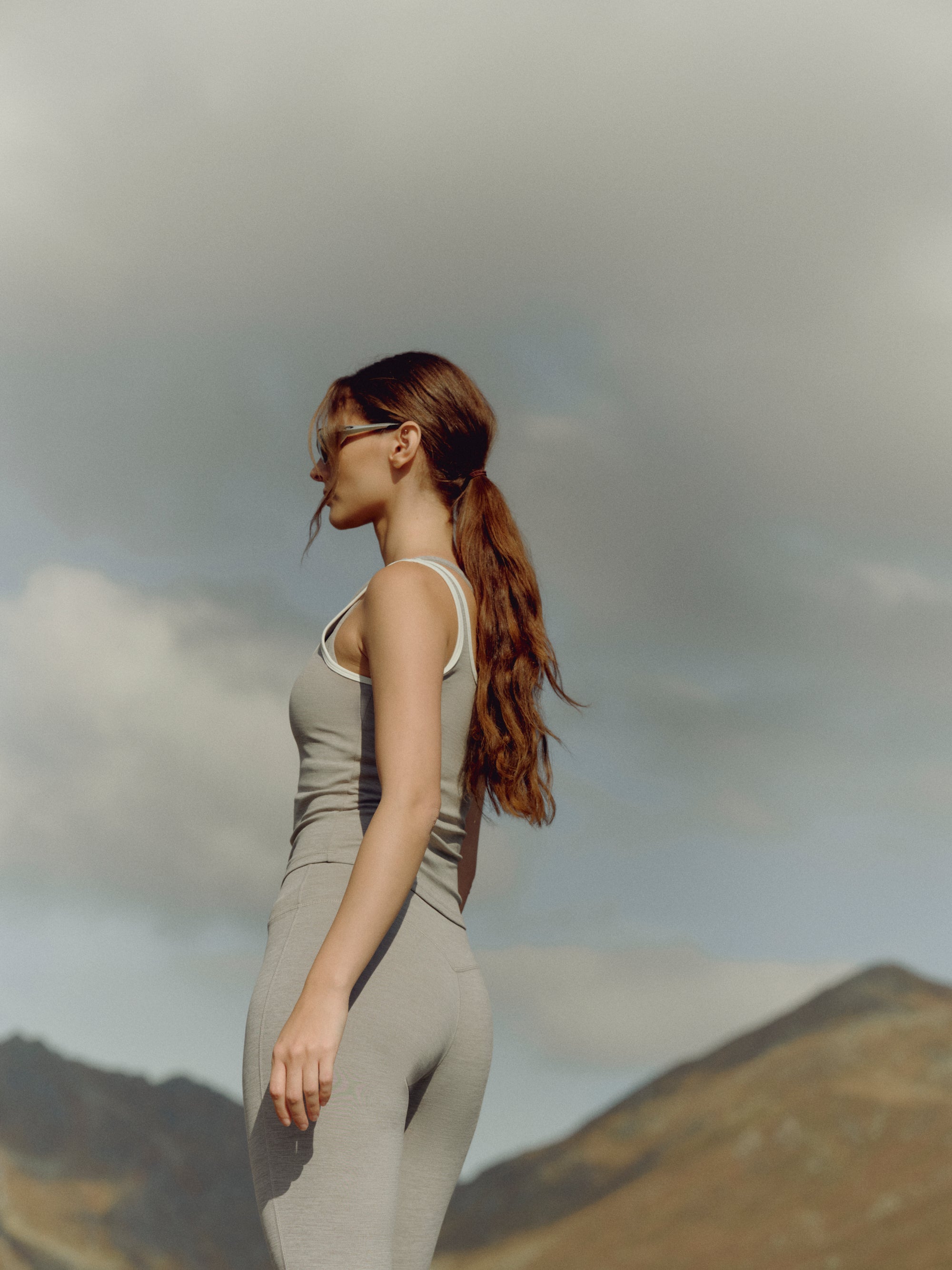 Woman wearing a grey melange CASPARA Cloudform square neck top outdoors in a mountain landscape.