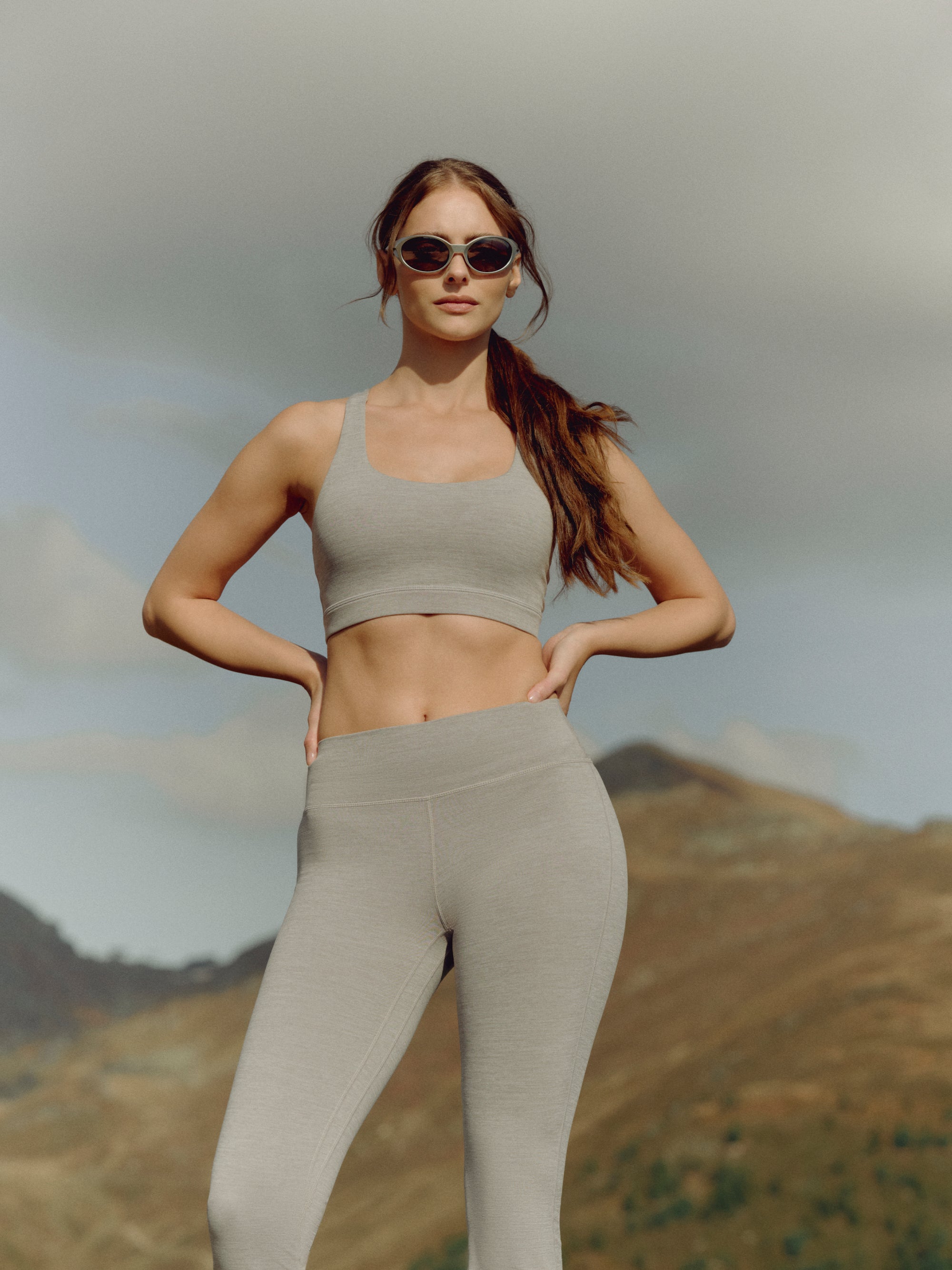 Woman wearing a grey melange CASPARA Cloudform sports bra in a mountain landscape.