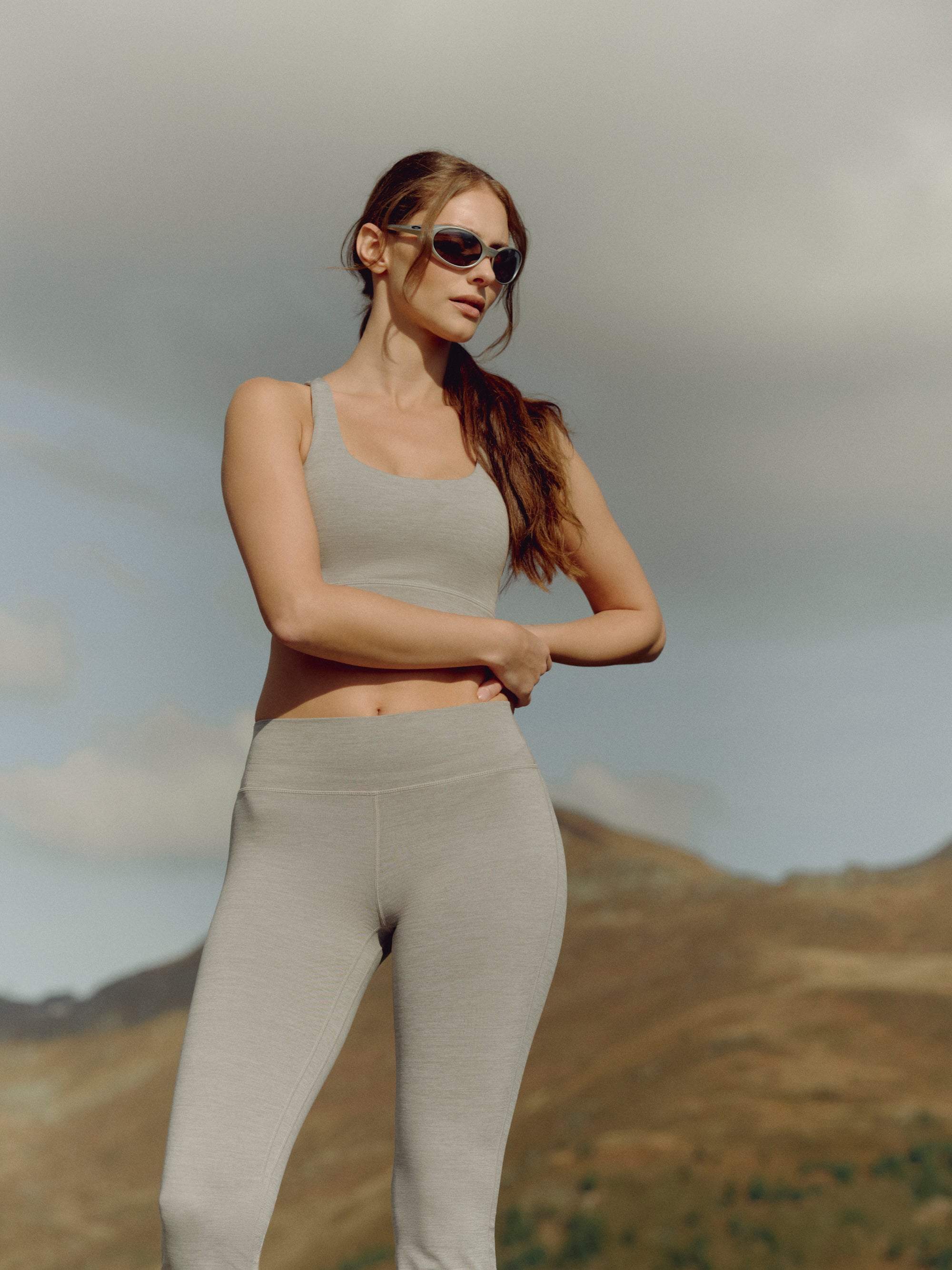 Woman wearing a grey melange CASPARA Cloudform sports bra in a mountain landscape.