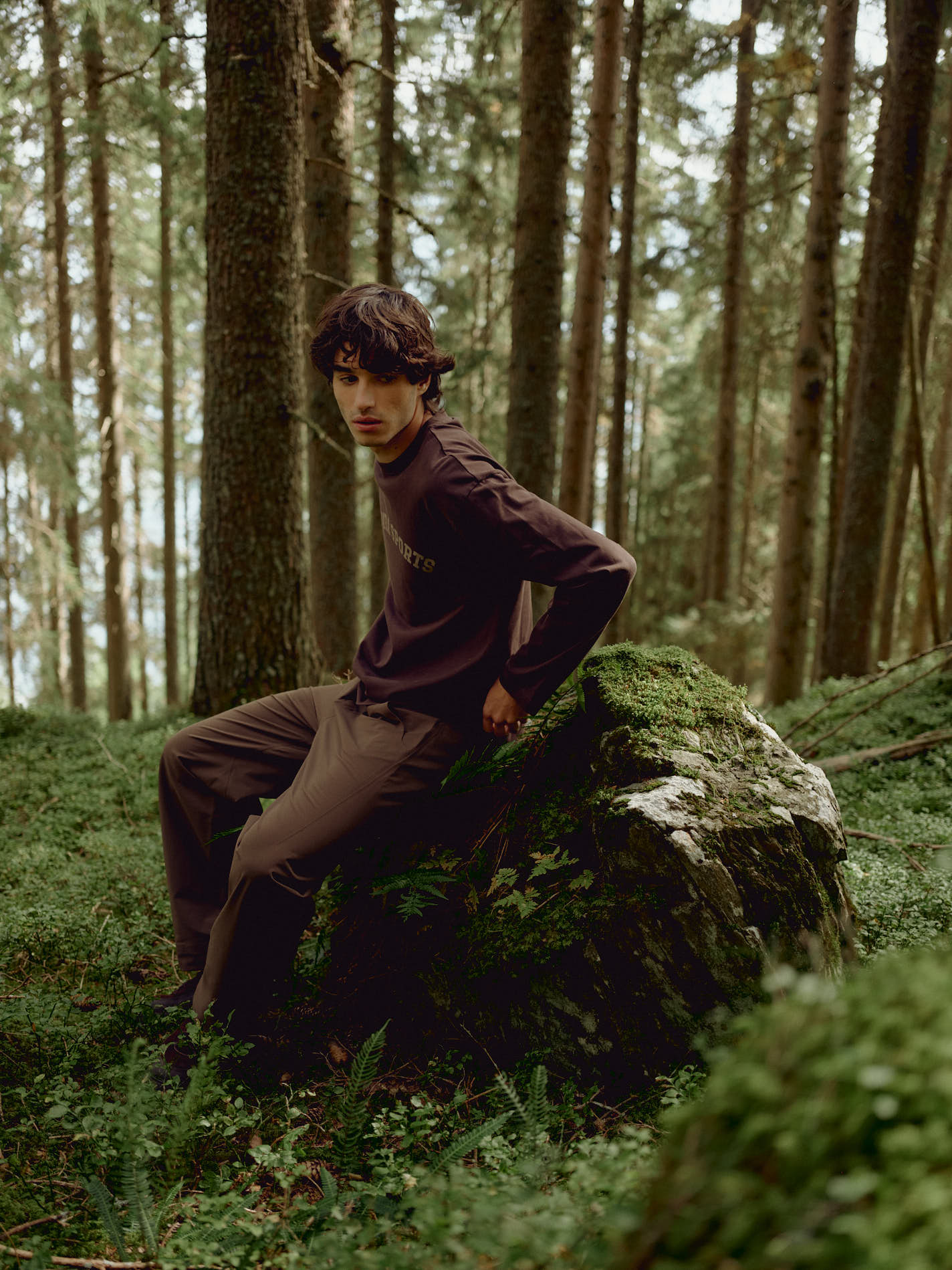 Man wearing an espresso CASPARA CS Signature long sleeve shirt sitting on a rock in a forest.