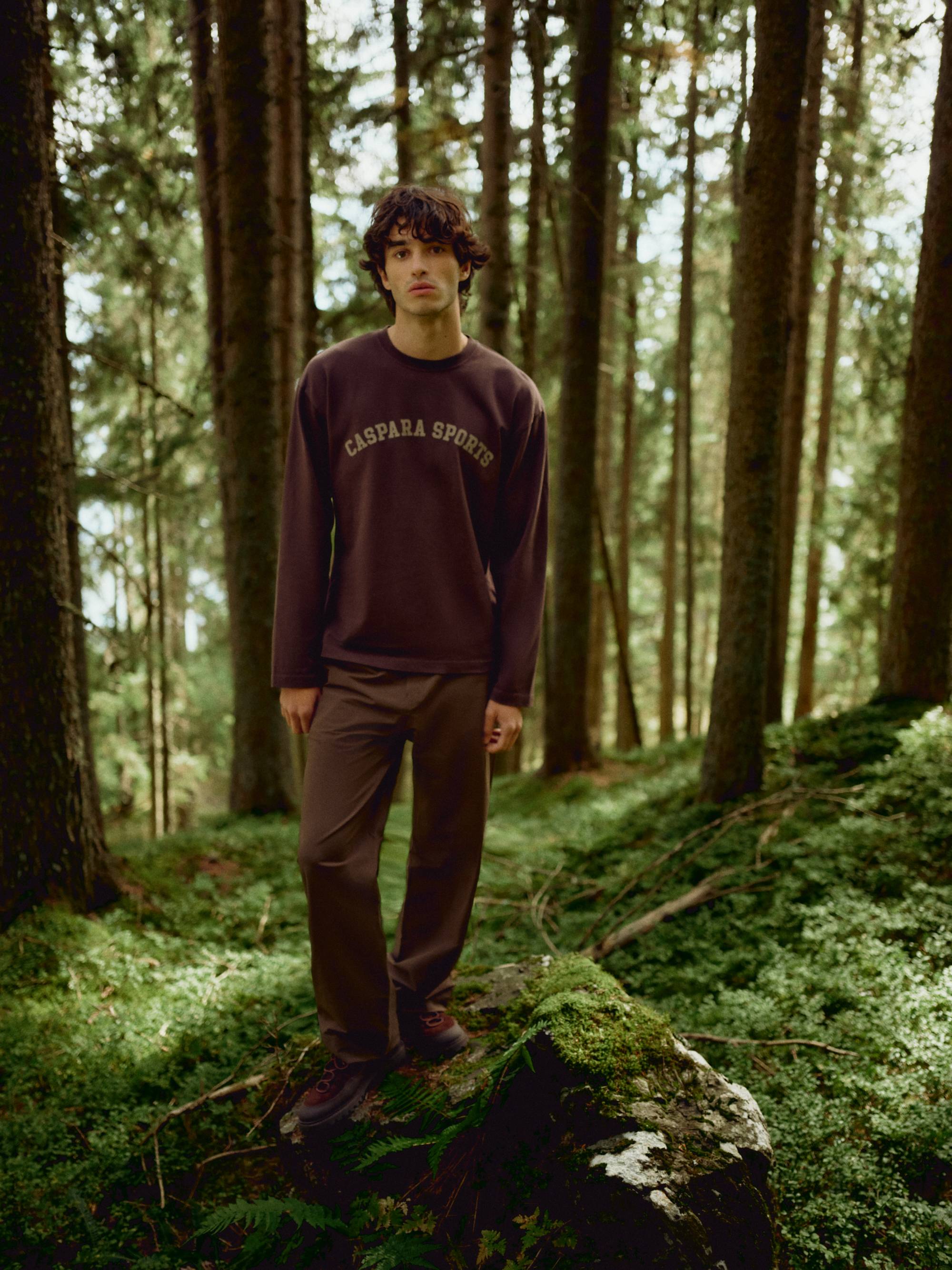 Man wearing an espresso CASPARA CS Signature long sleeve shirt standing in a forest.