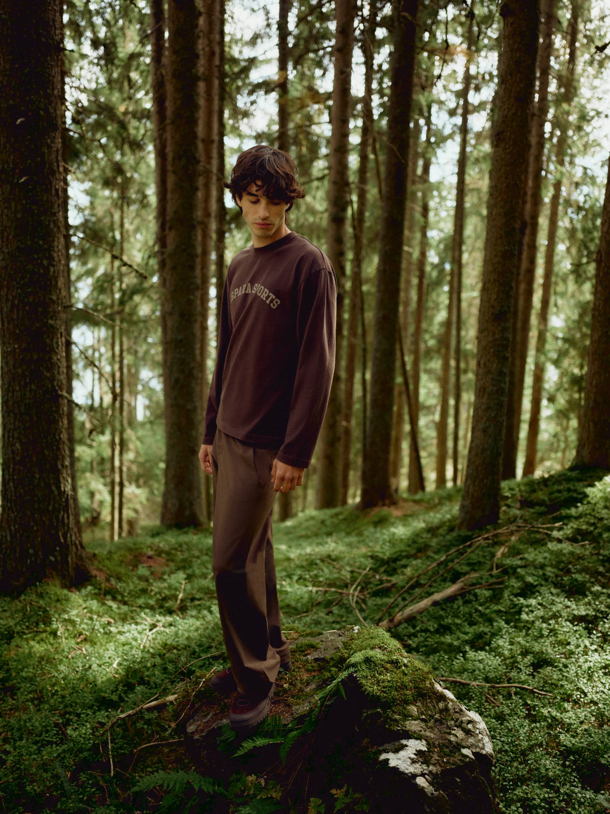 Man wearing an espresso CASPARA CS Signature long sleeve shirt in a sunlit forest.