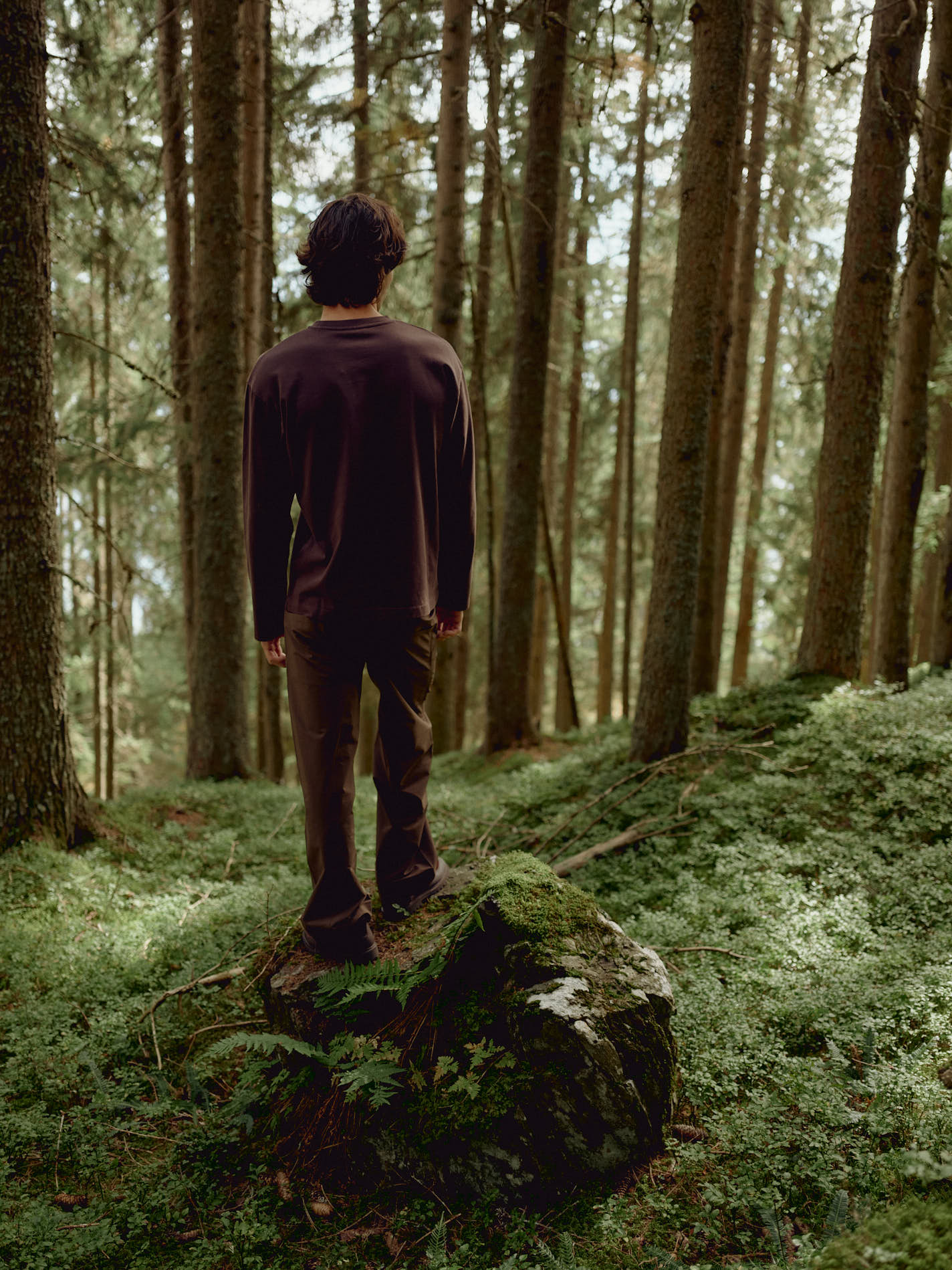 Man wearing an espresso CASPARA CS Signature long sleeve shirt standing on a mossy rock in a forest.