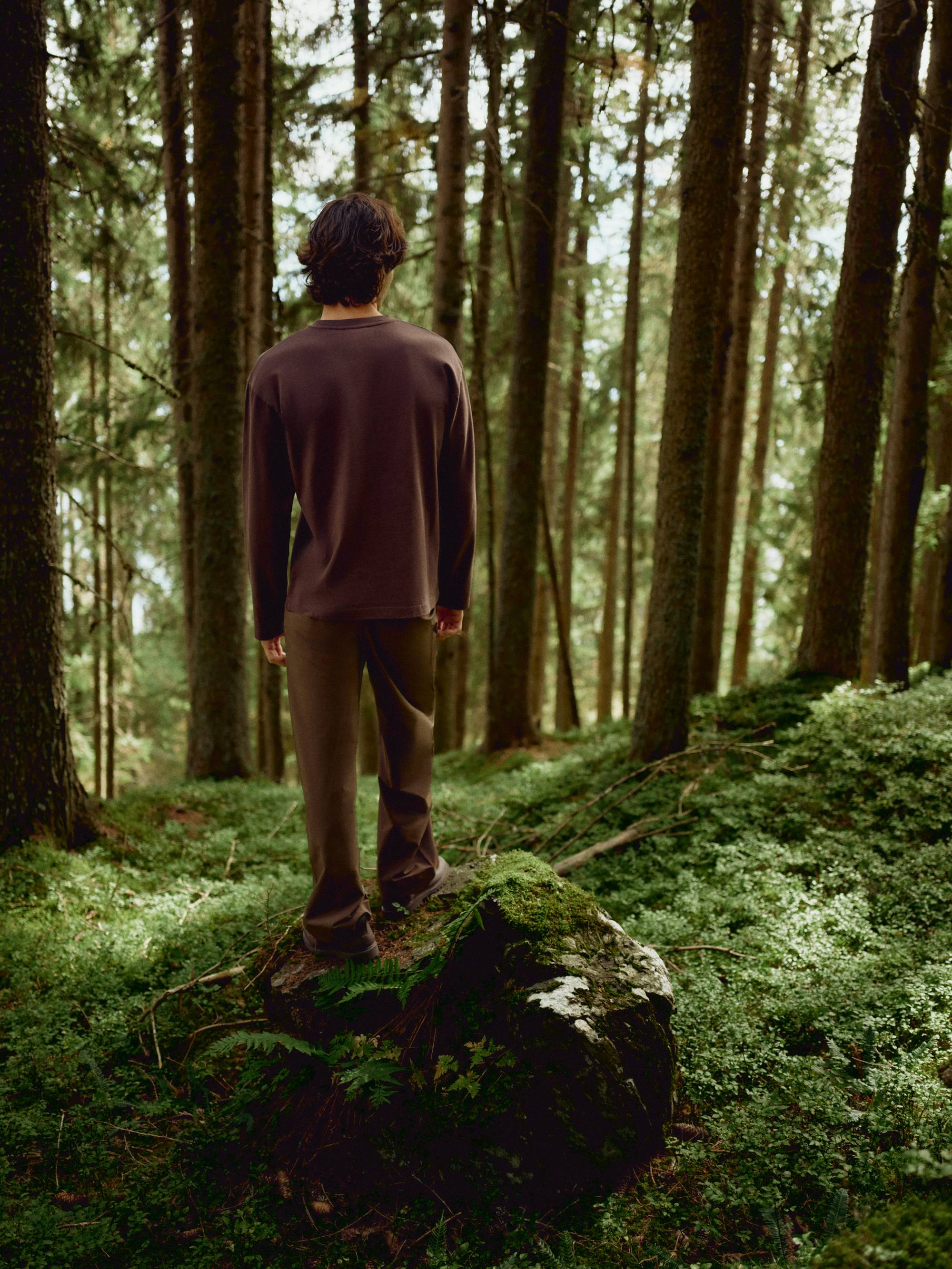 Man seen from behind wearing an espresso CASPARA CS Signature long sleeve shirt in a forest.