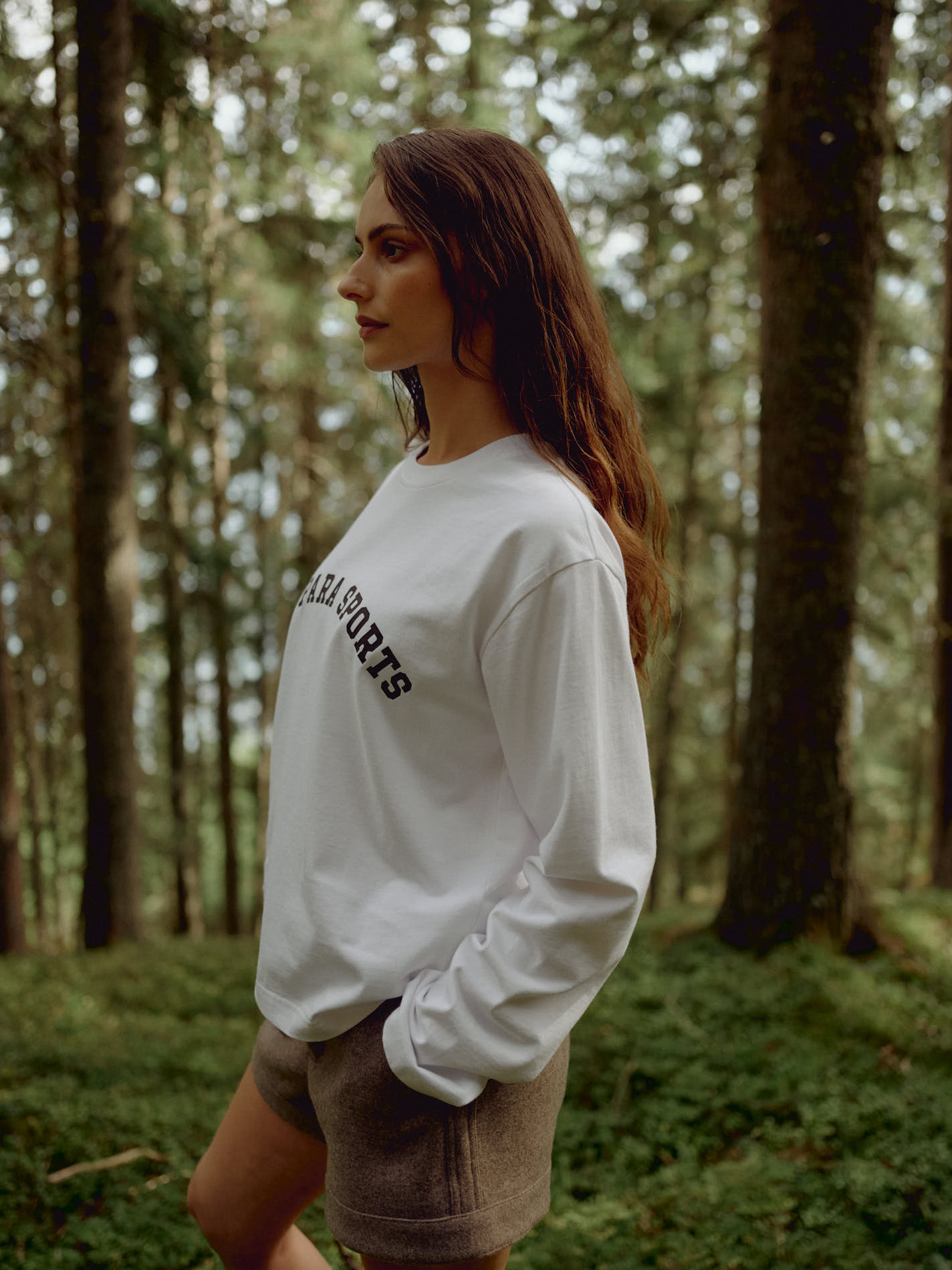 Woman wearing a white CASPARA CS Signature long sleeve shirt standing in a pine forest.