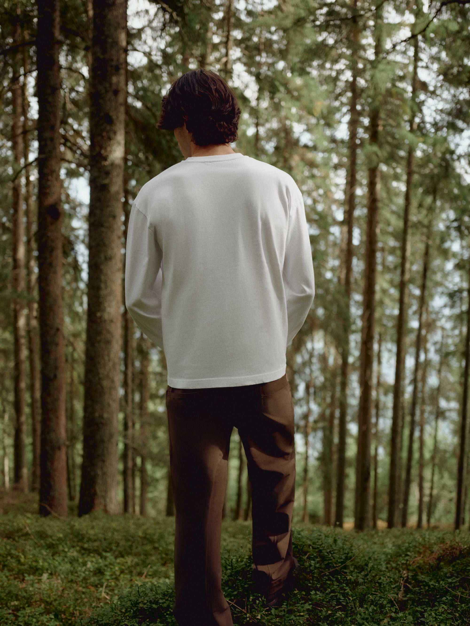 Man seen from behind wearing a white CASPARA CS Signature long sleeve shirt in a forest.