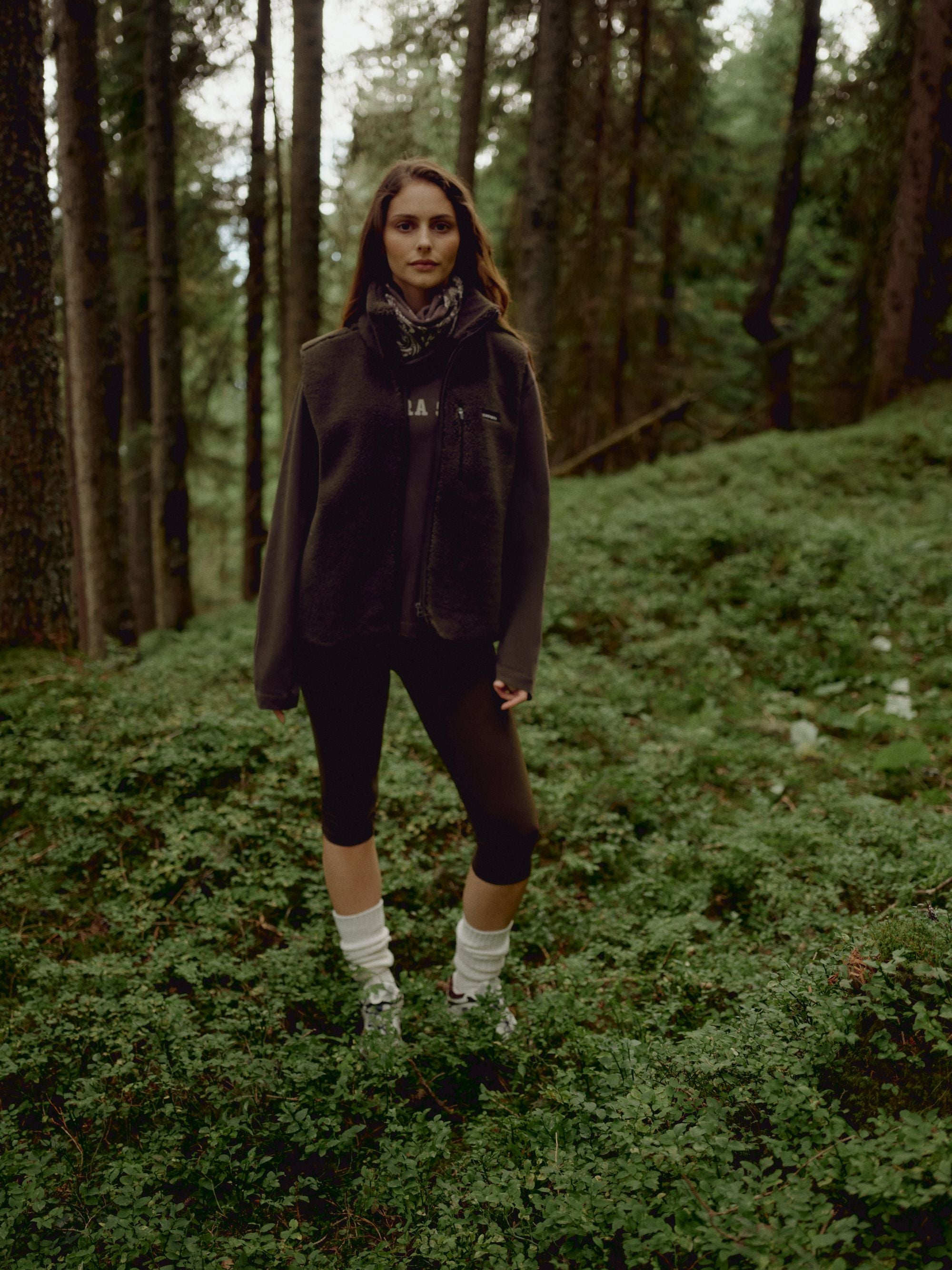 Woman wearing a khaki CASPARA Cloudfleece vest standing in a forest.