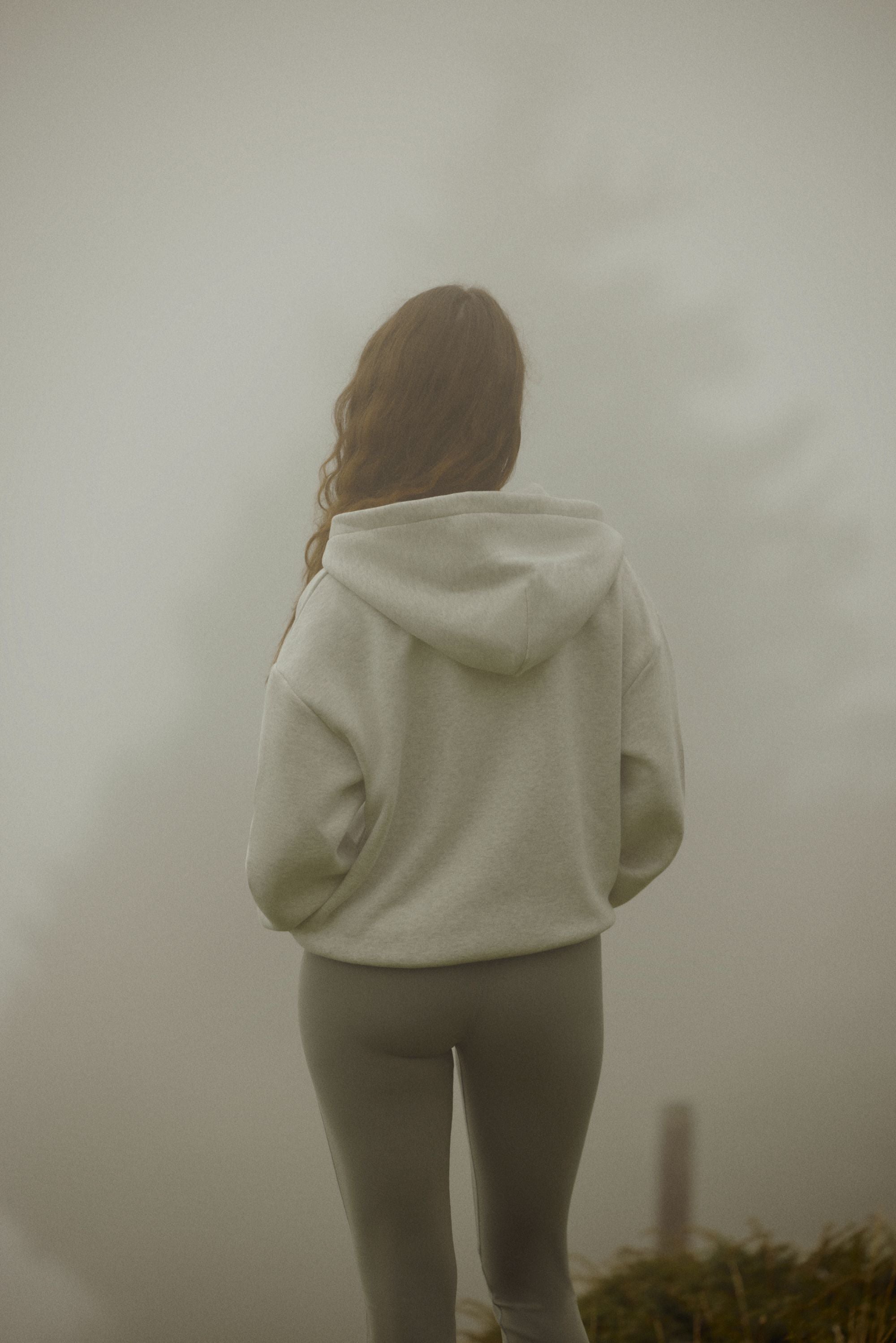 Woman wearing a grey melange CASPARA CS zip hoodie standing in a foggy landscape.