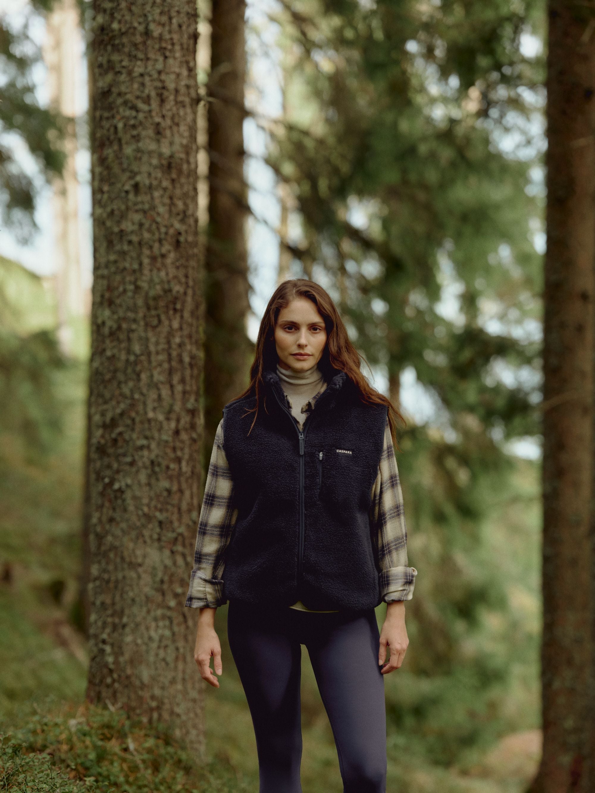Woman wearing a navy CASPARA Cloudfleece vest standing in a forest.