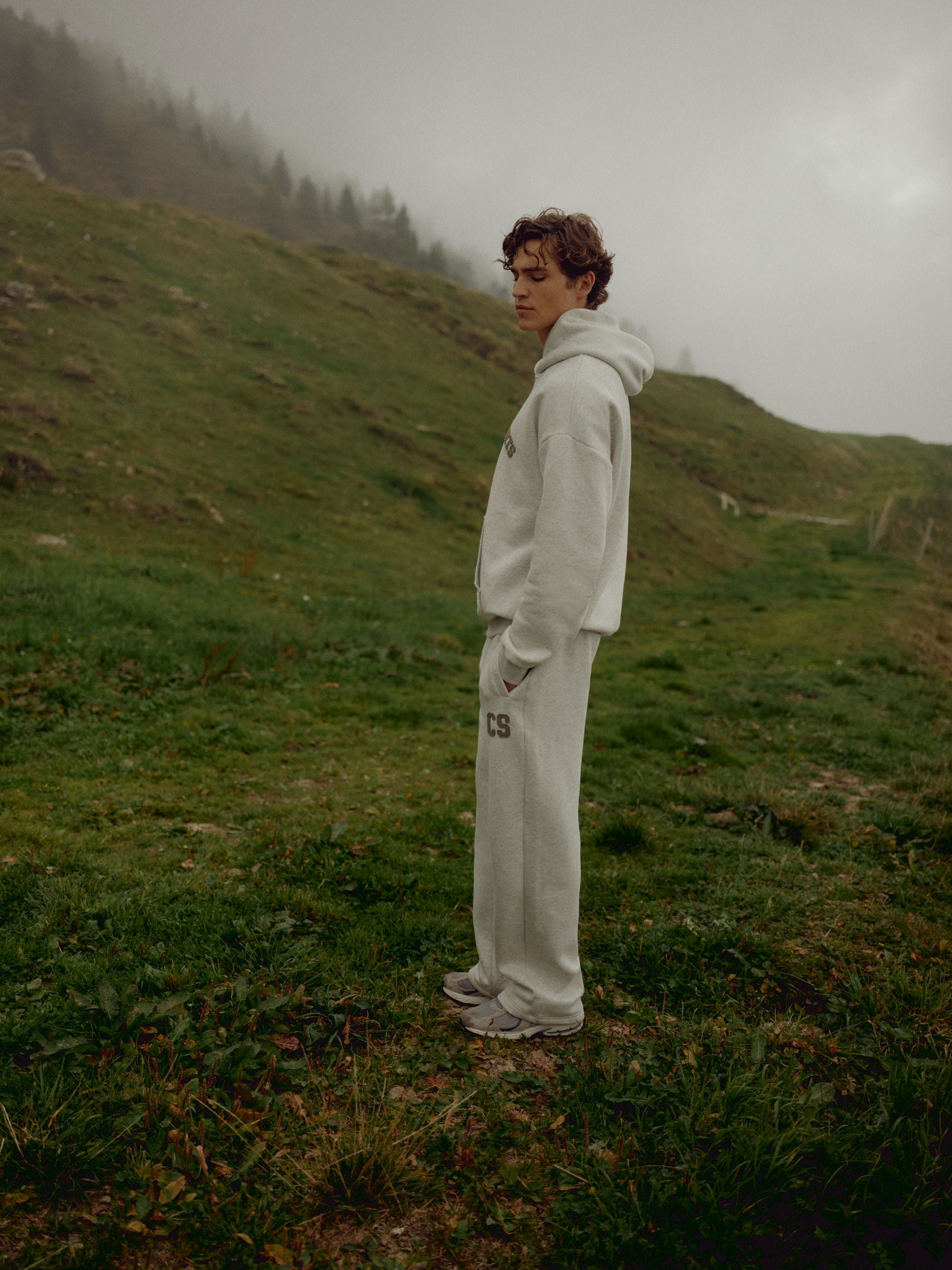 Man wearing a grey melange CASPARA CS hoodie standing on a foggy hillside.