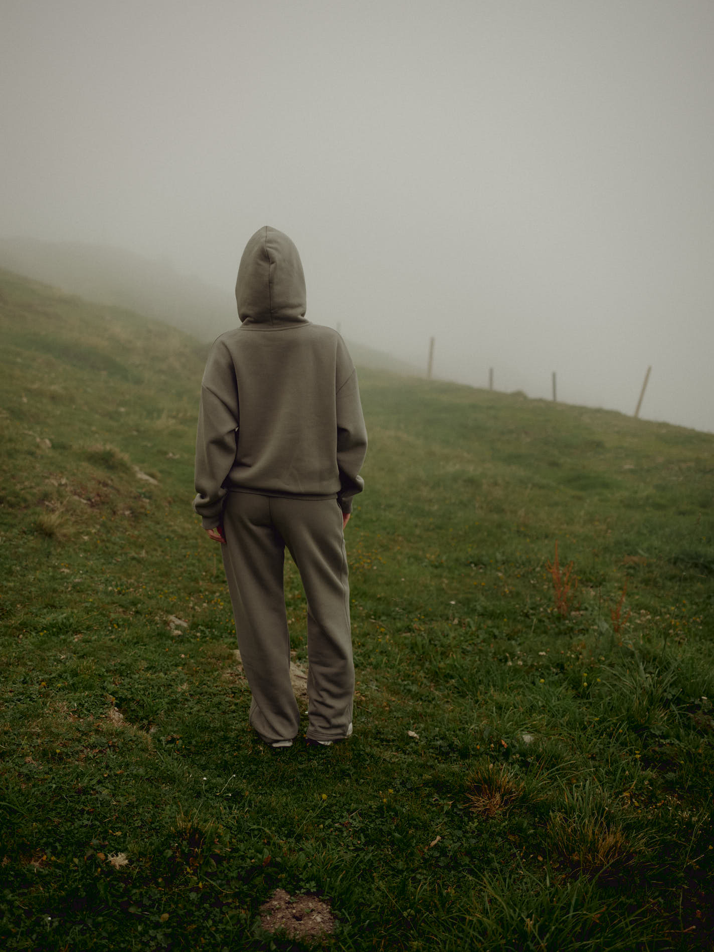 Woman wearing a khaki CASPARA CS hoodie standing in a foggy, grassy landscape.