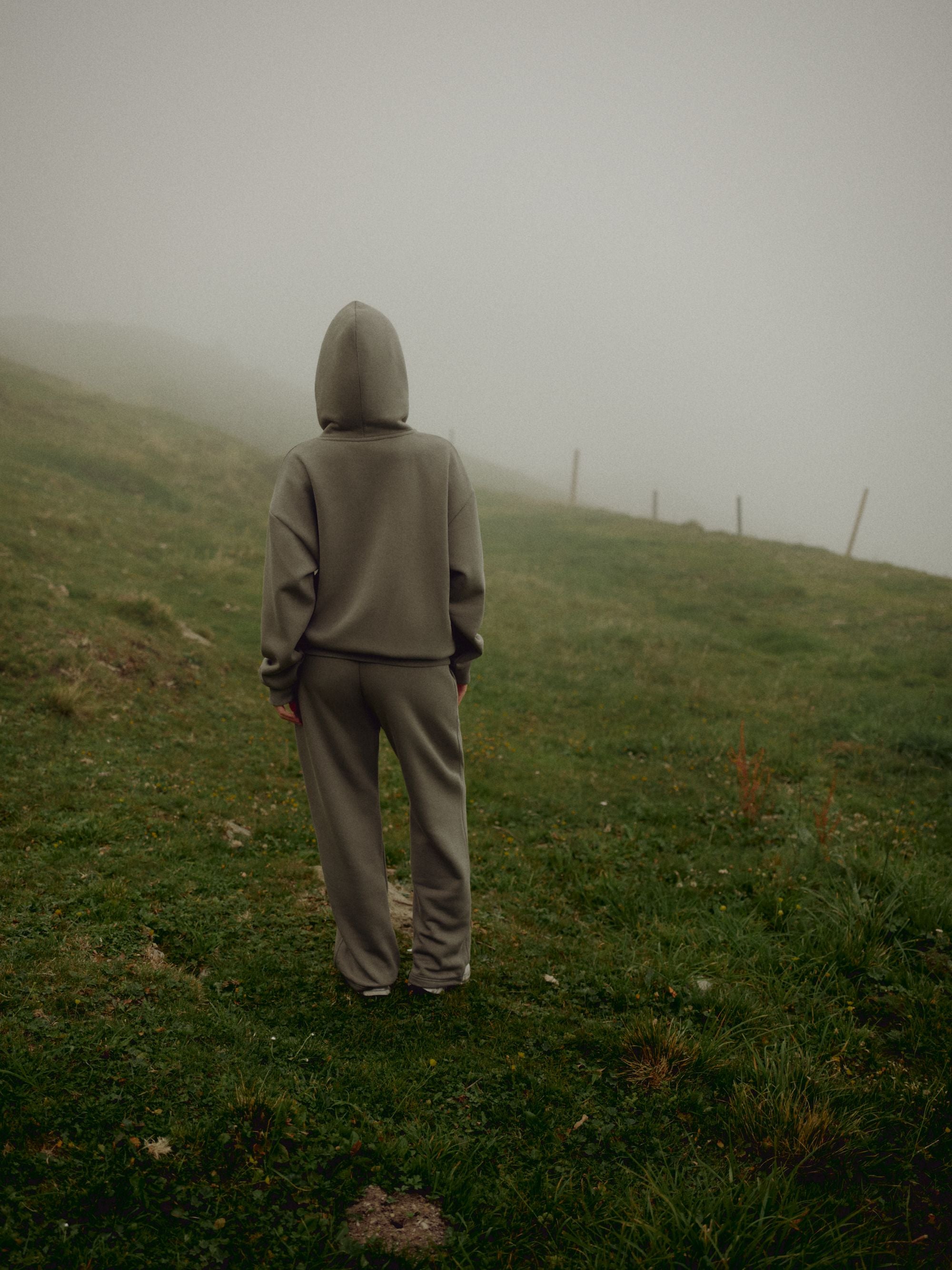 Woman wearing a khaki CASPARA CS hoodie and sweatpants on a misty hillside.