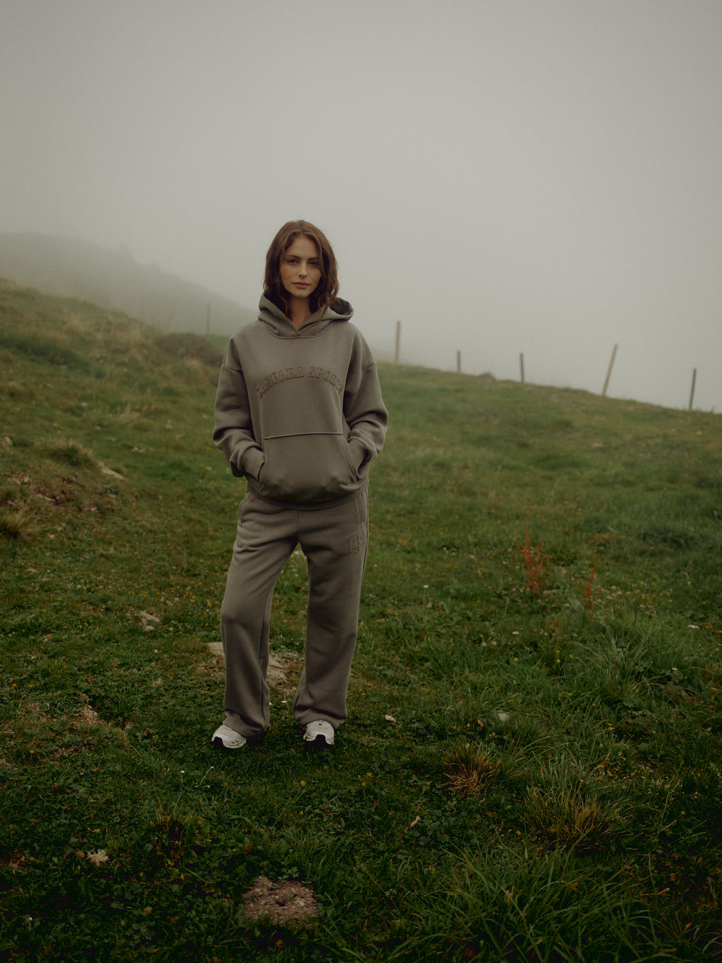 Woman wearing a khaki CASPARA CS hoodie and matching sweatpants on a misty hillside.