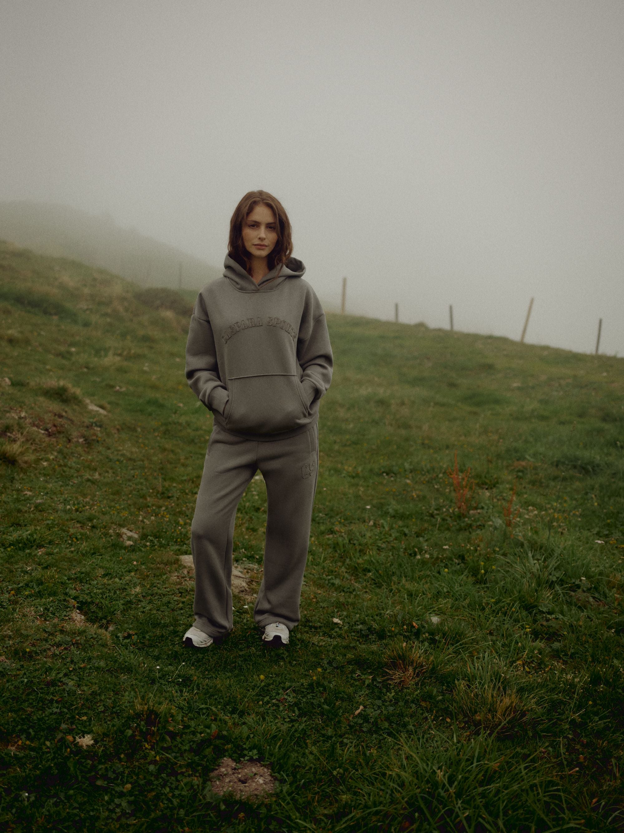 Woman wearing a khaki CASPARA CS hoodie and sweatpants on a foggy hillside.