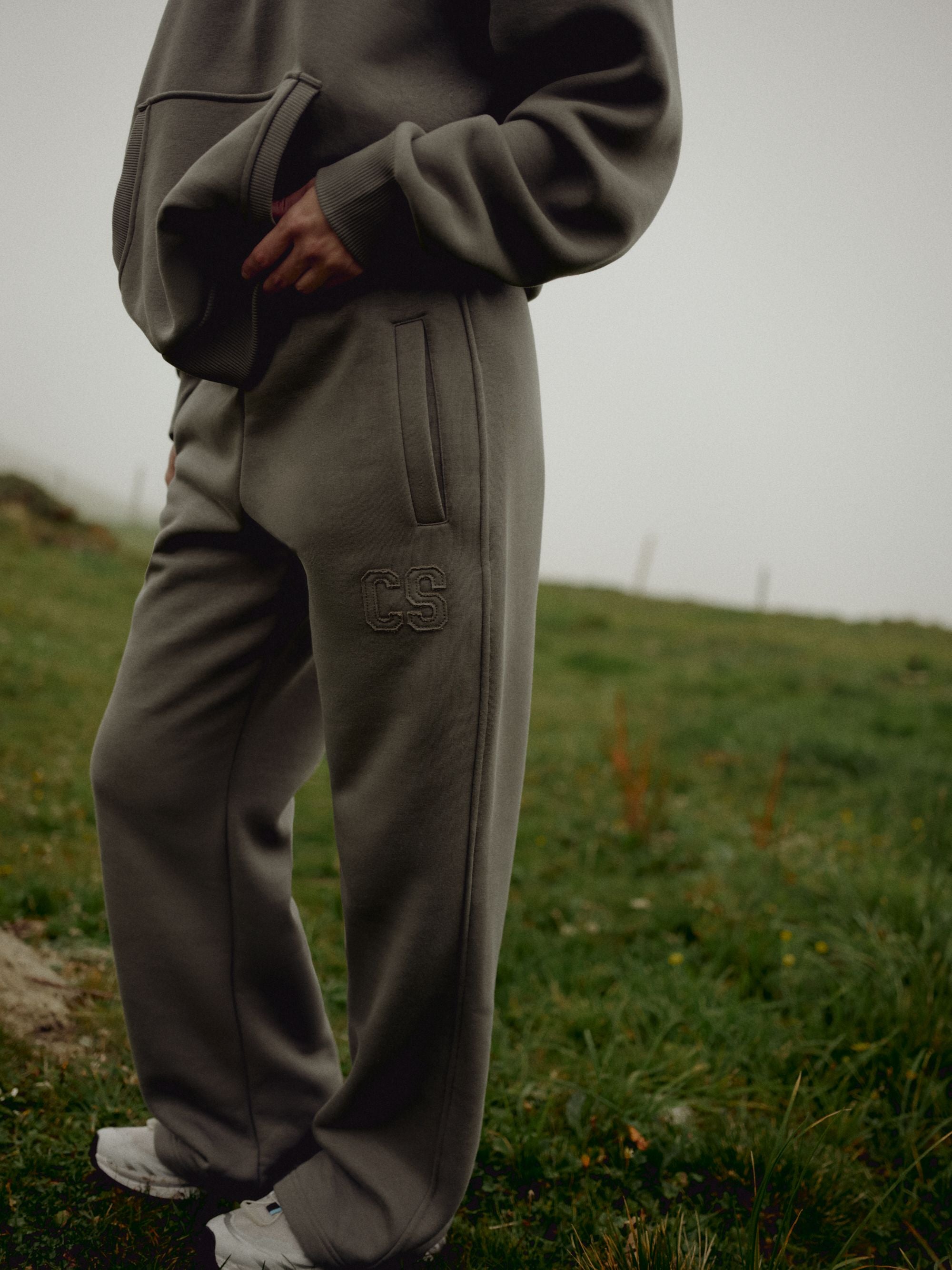 Woman wearing khaki CASPARA CS SL sweatpants standing in a grassy landscape.