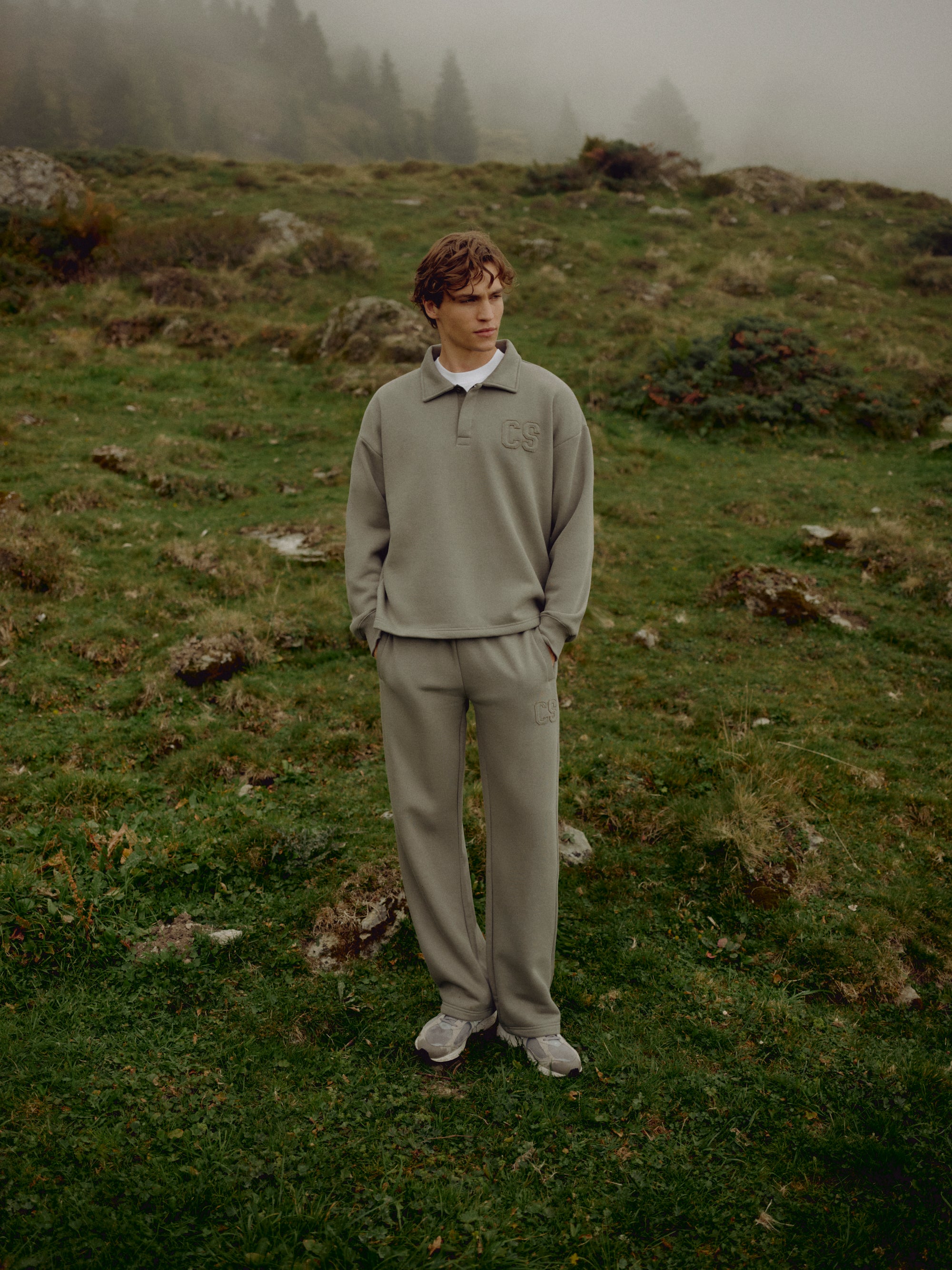 Man wearing khaki CASPARA CS sweatpants standing in a misty mountain landscape.
