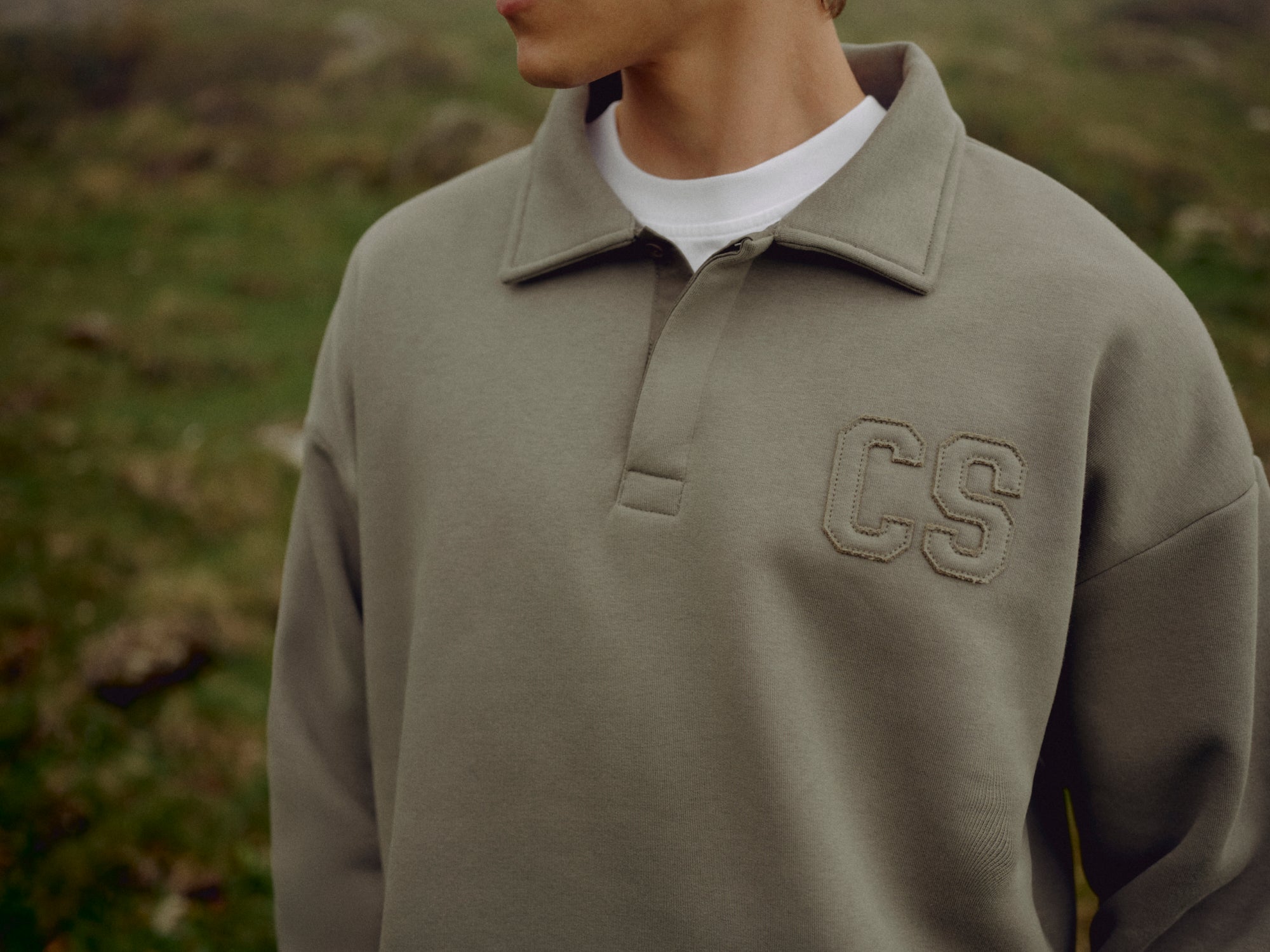 Close-up of a man wearing a khaki CASPARA CS rugby shirt outdoors.