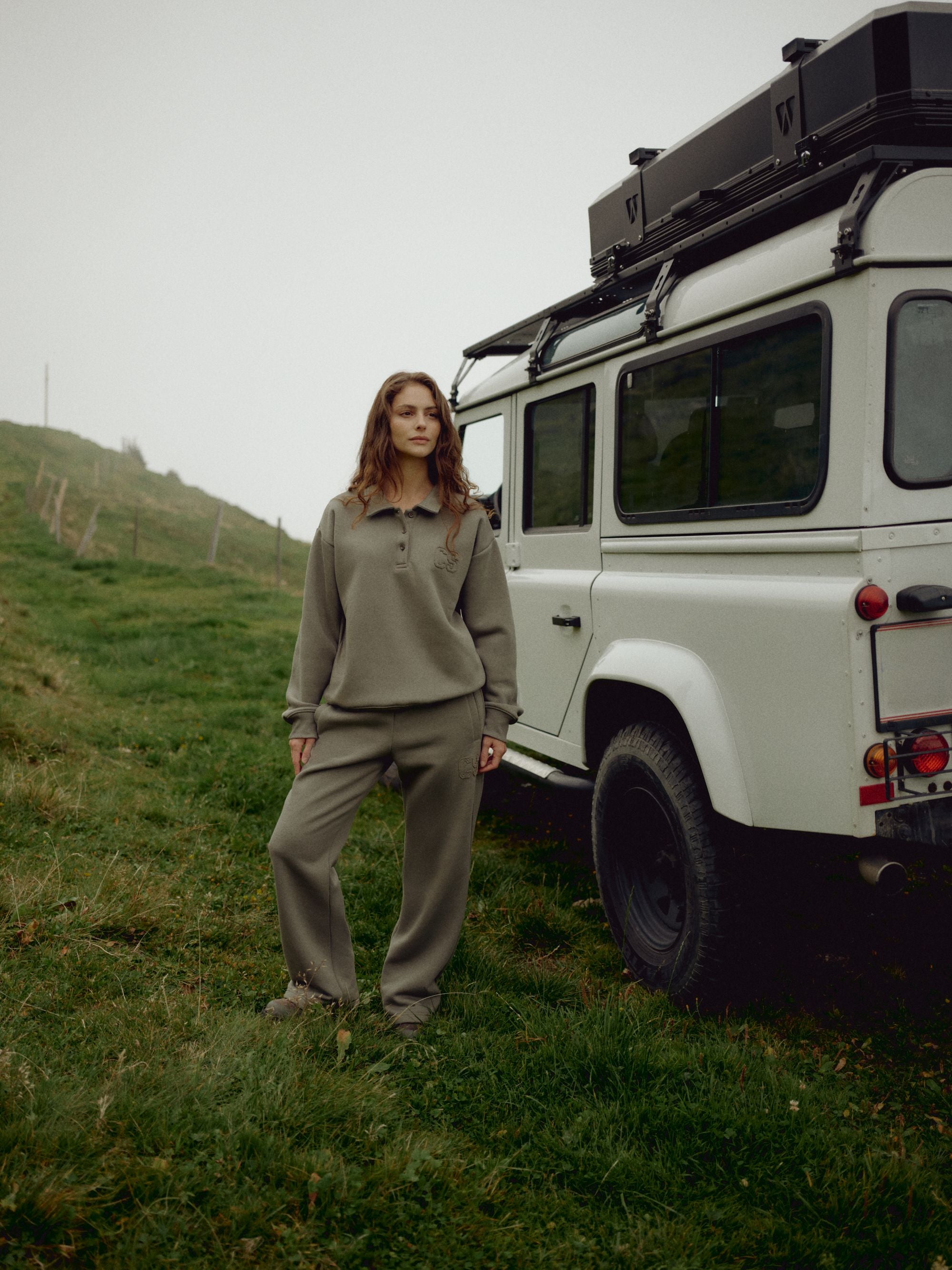 Woman wearing a khaki CASPARA CS rugby shirt and sweatpants standing next to an off-road vehicle.