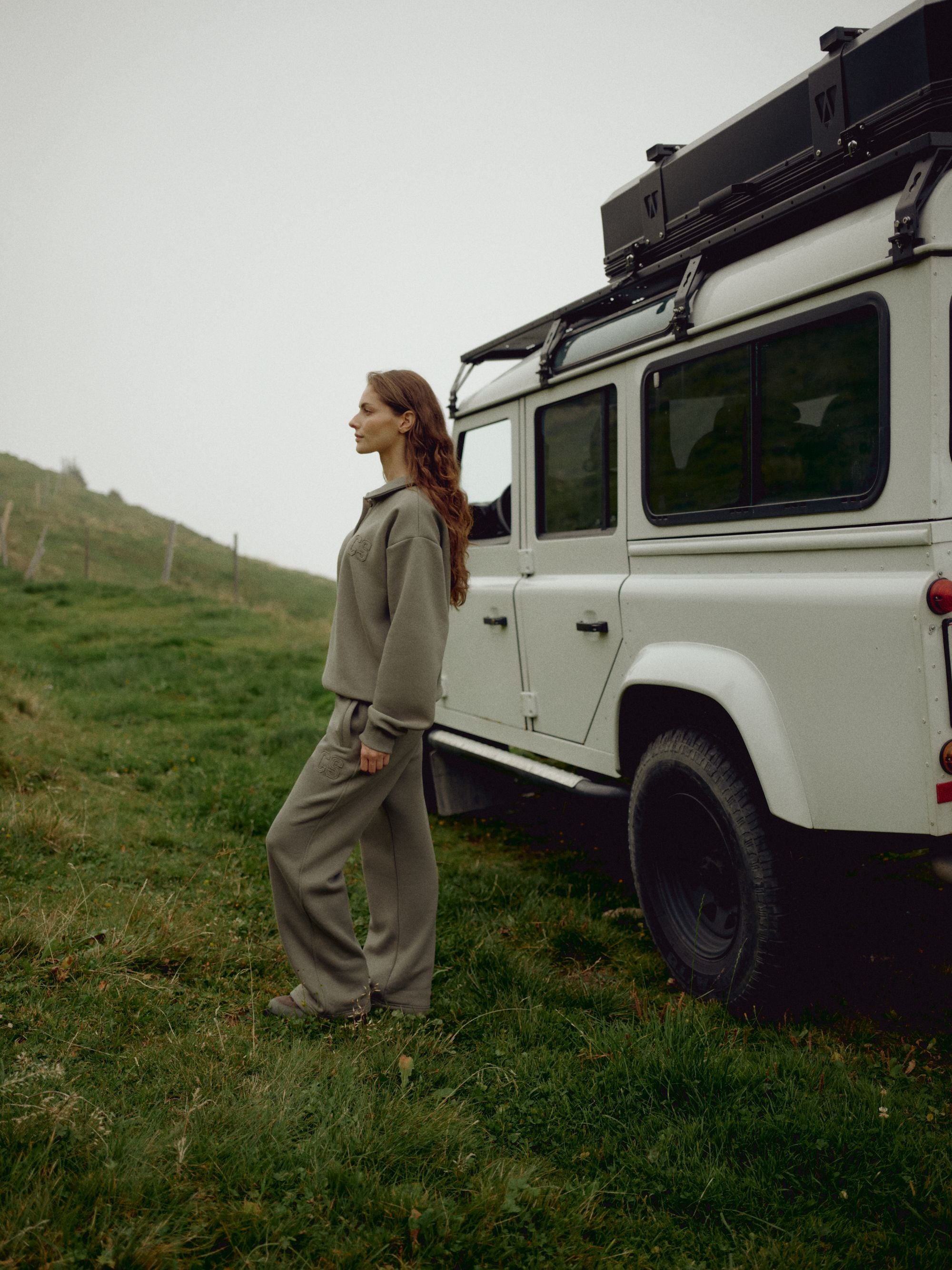 Woman wearing a khaki CASPARA CS rugby shirt and sweatpants next to an off-road vehicle.