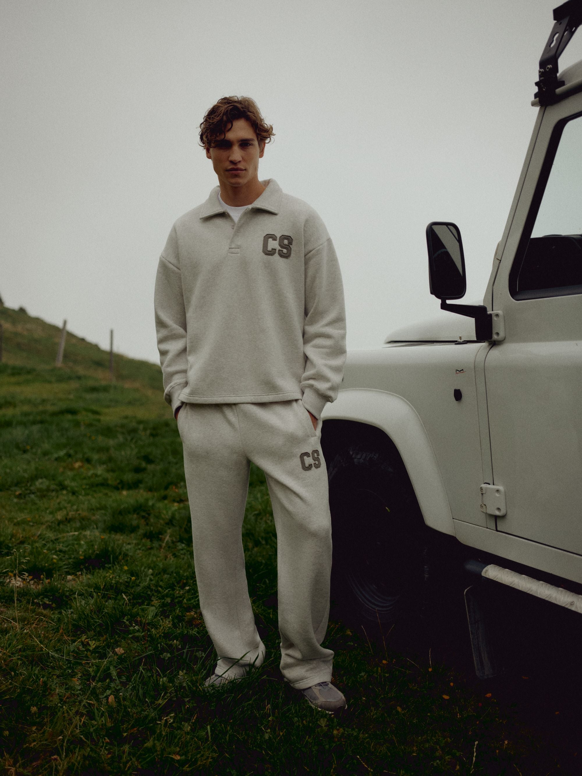 Man wearing a grey melange CASPARA CS rugby shirt and sweatpants next to an off-road vehicle.