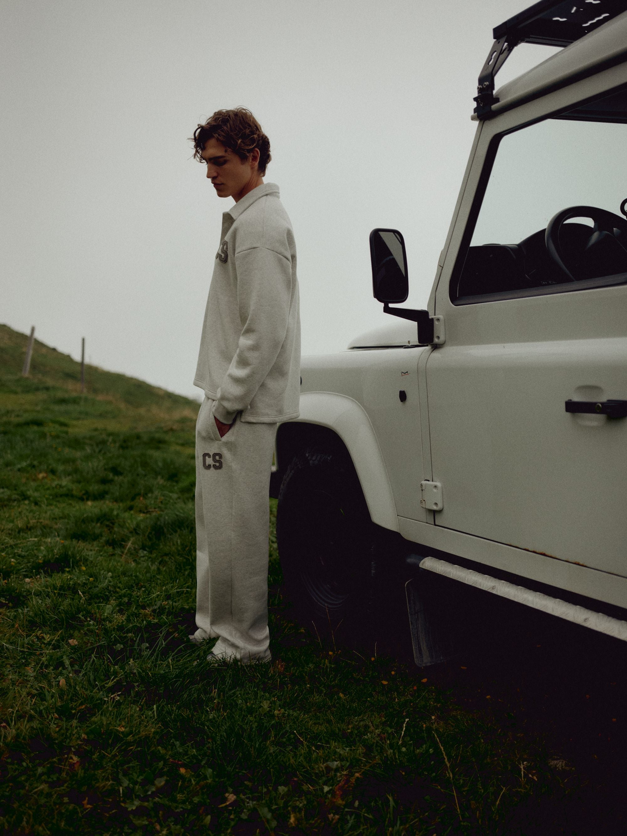 Man wearing a grey melange CASPARA rugby shirt and sweatpants beside a white off-road vehicle.