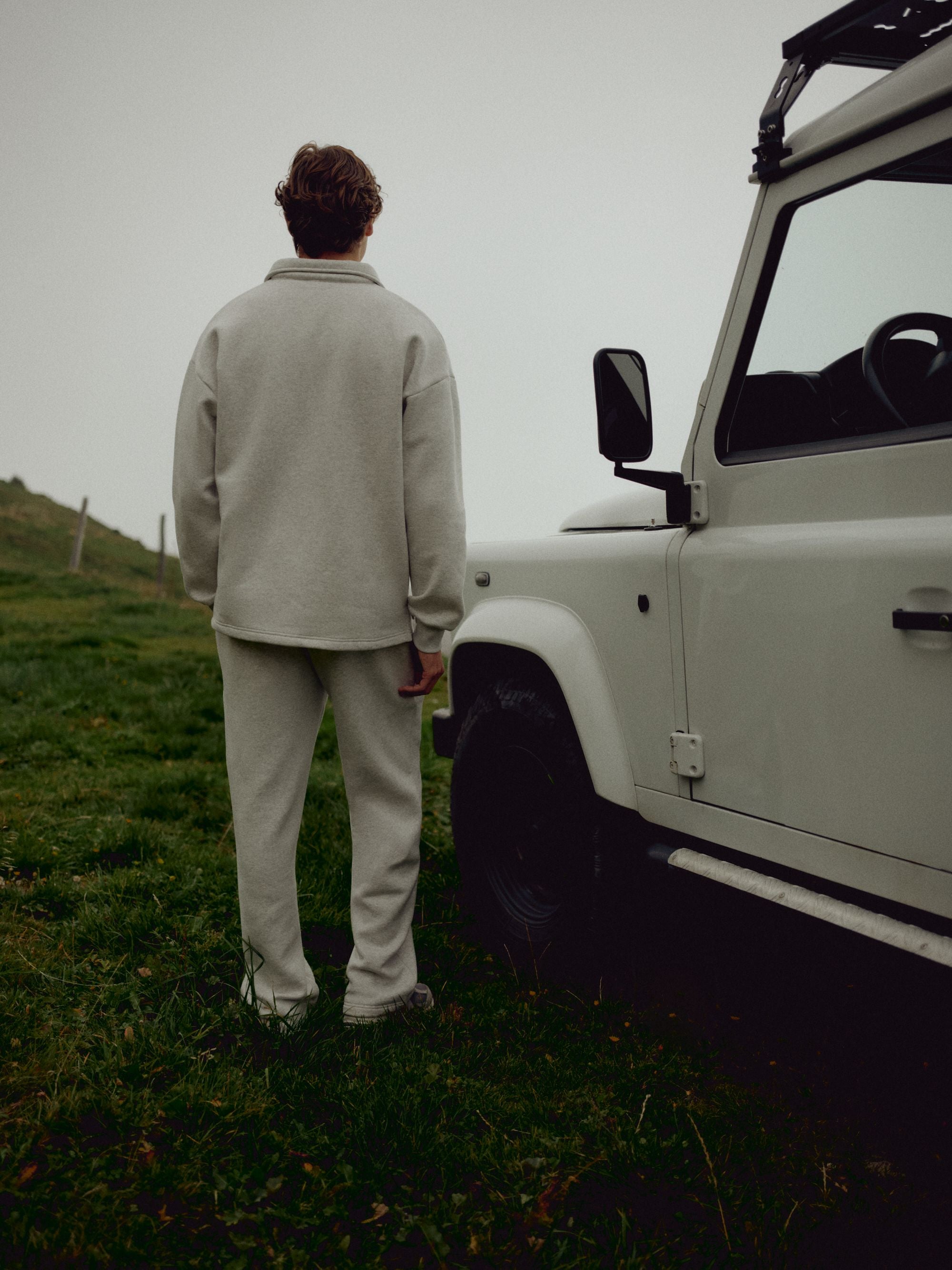 Man wearing a grey melange CASPARA rugby shirt and sweatpants beside a white off-road vehicle.