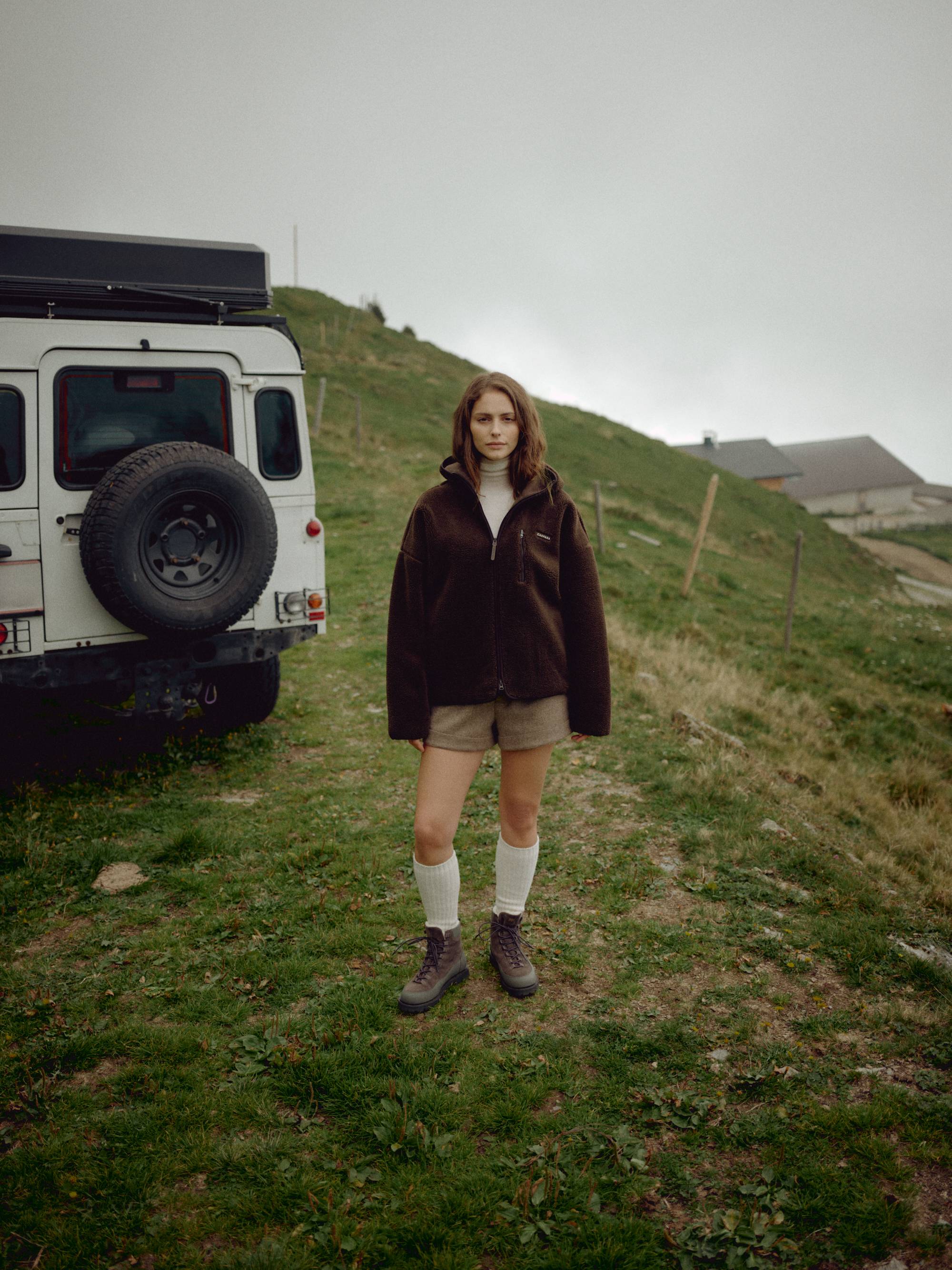 Woman wearing an espresso CASPARA Cloudfleece jacket standing next to an off-road vehicle.