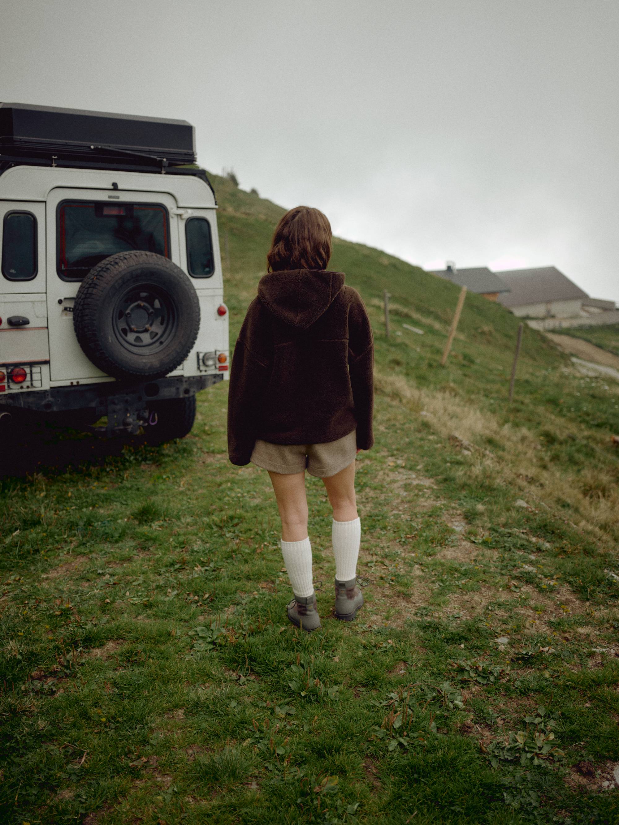 Woman wearing an espresso CASPARA Cloudfleece hooded jacket next to a vehicle on a hillside.