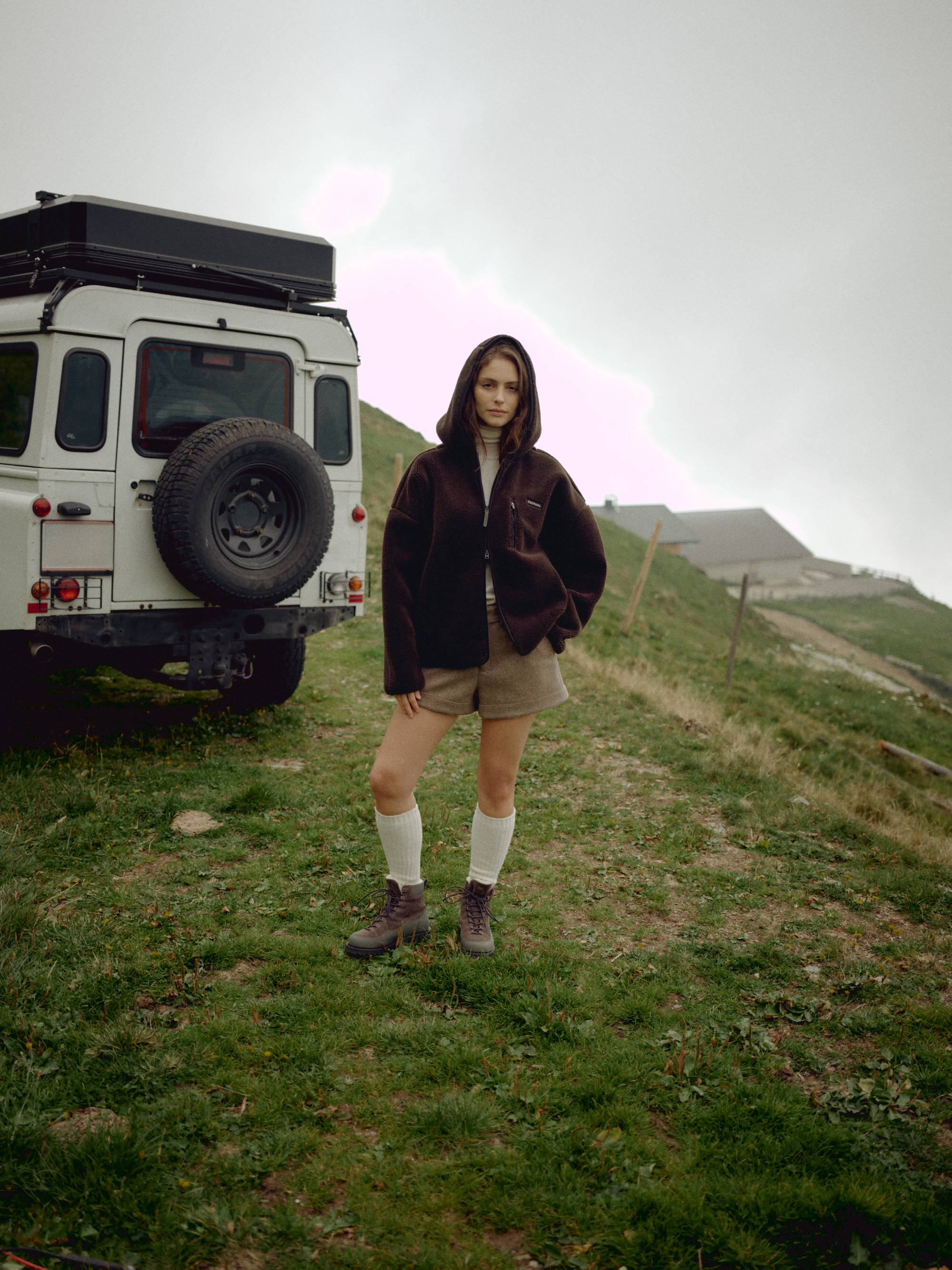Woman wearing an espresso CASPARA Cloudfleece hooded jacket next to an off-road vehicle.