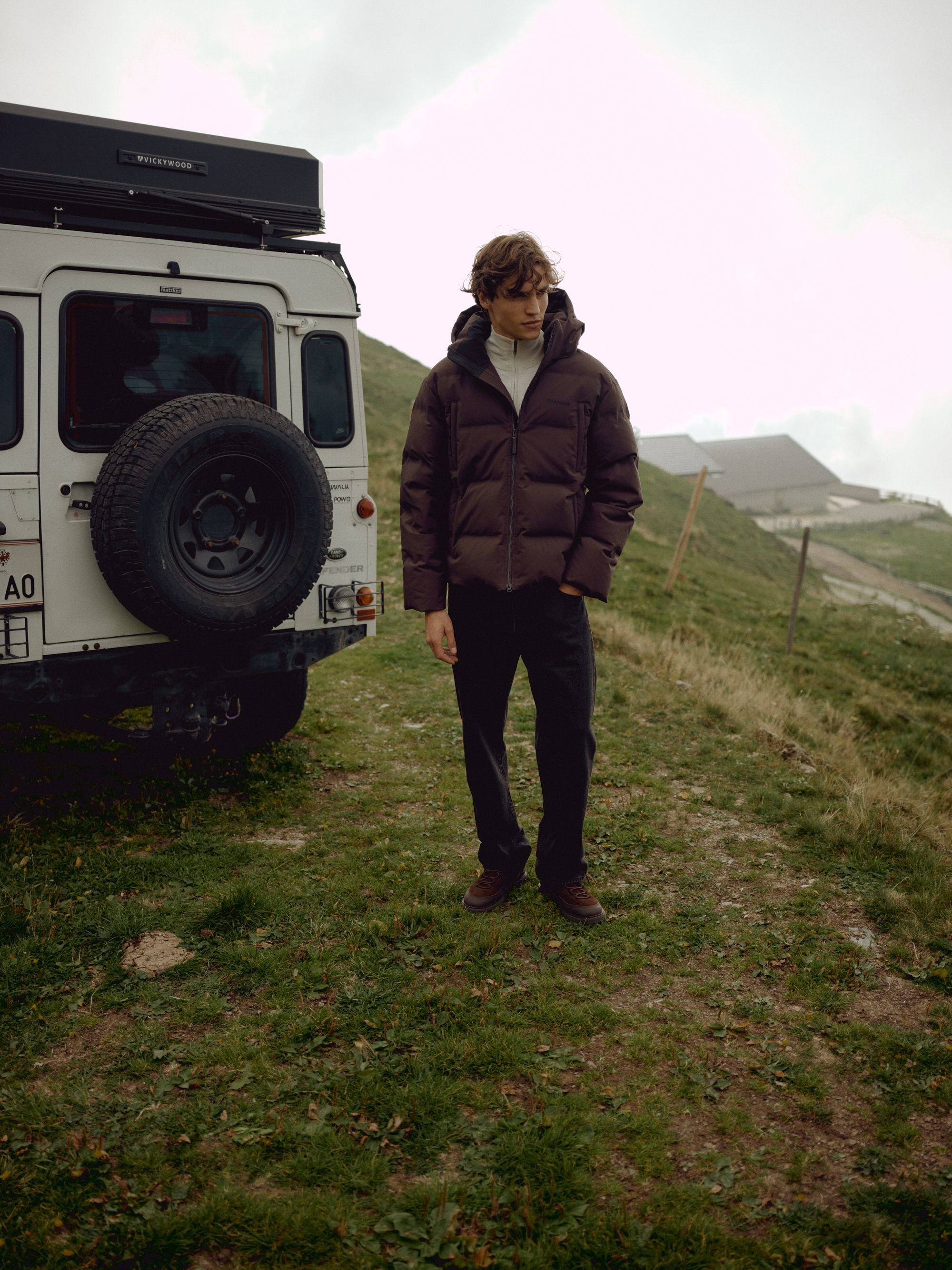 Man wearing a cocoa bean CASPARA Boreal puffer jacket outdoors next to an off-road vehicle.