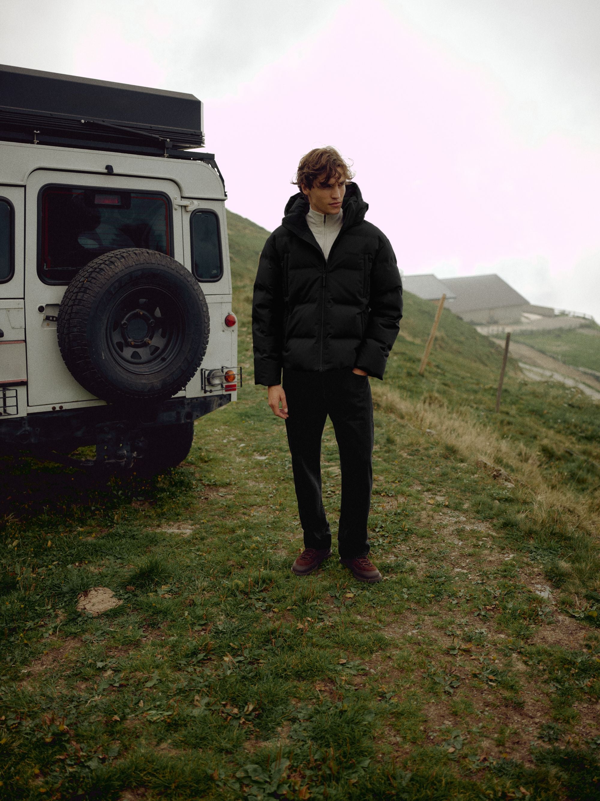 Man wearing a black CASPARA Boreal puffer jacket standing next to an off-road vehicle outdoors.