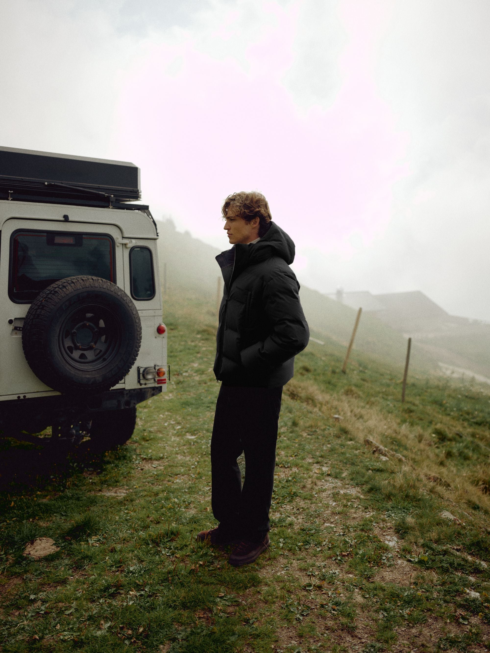 Man wearing a black CASPARA Boreal puffer jacket outdoors next to an off-road vehicle.