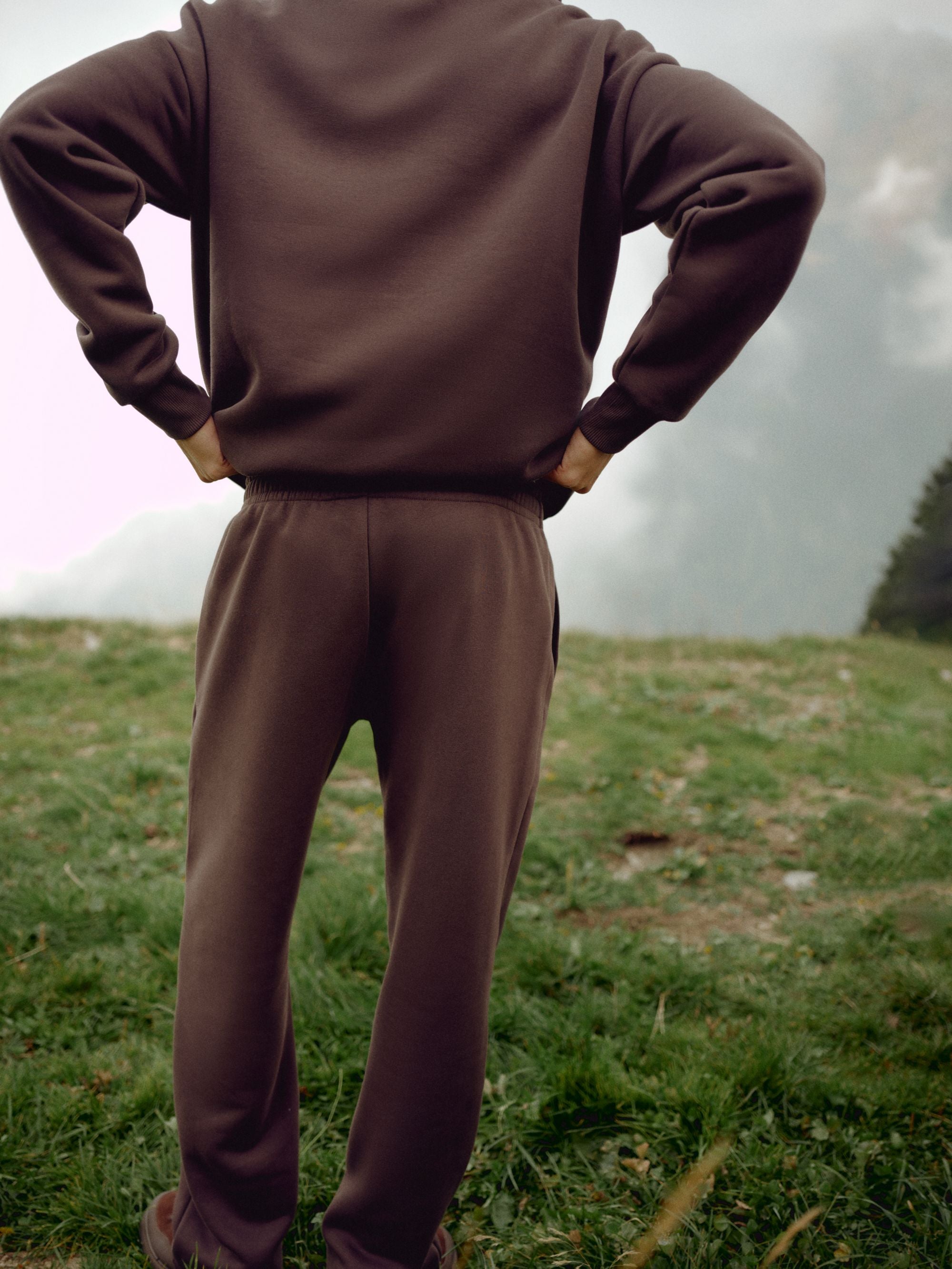 Back view of a man wearing espresso CASPARA CS sweatpants on a grassy hillside.