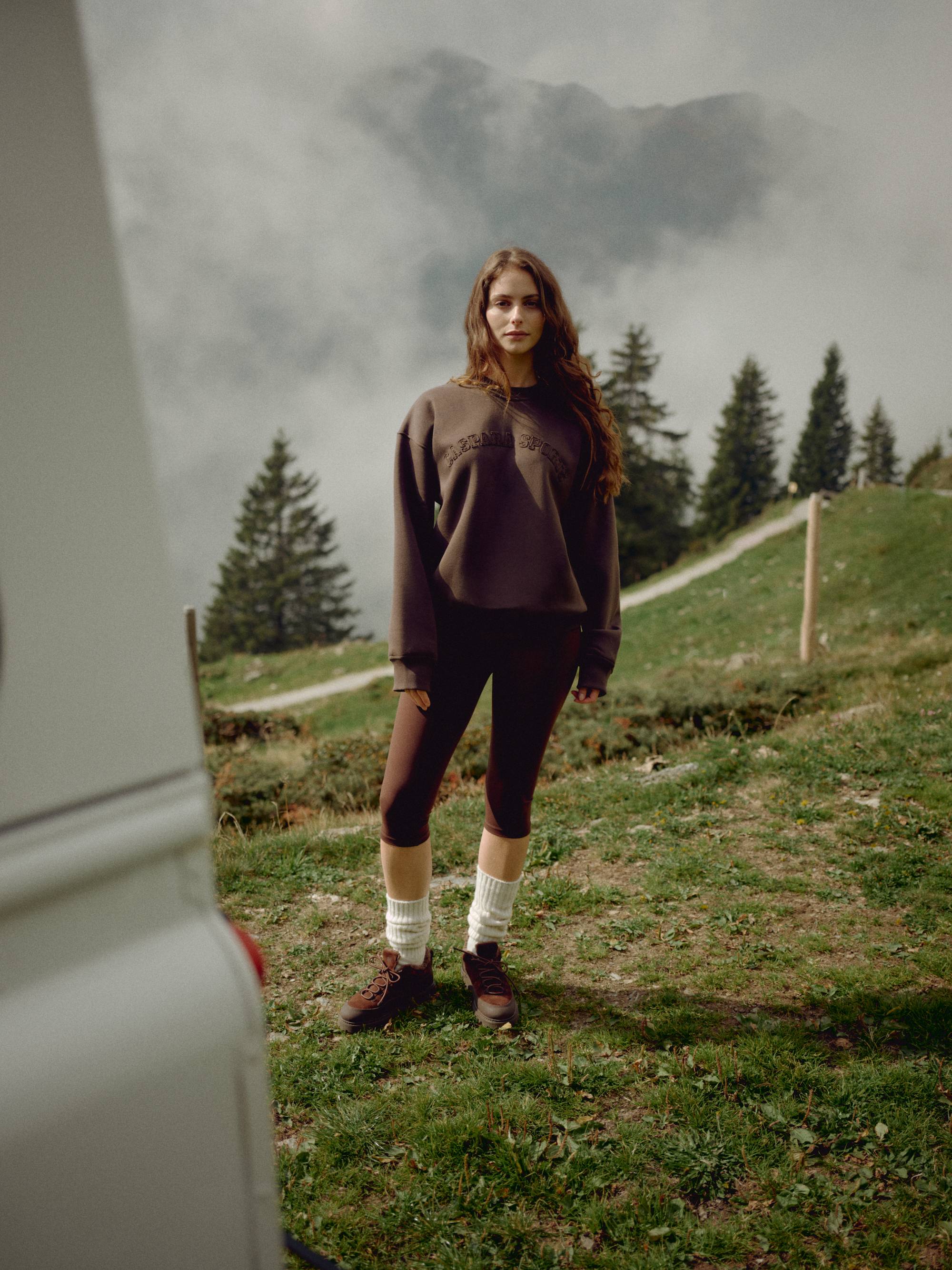 Woman wearing an espresso CASPARA CS crewneck sweatshirt in a misty mountain landscape.