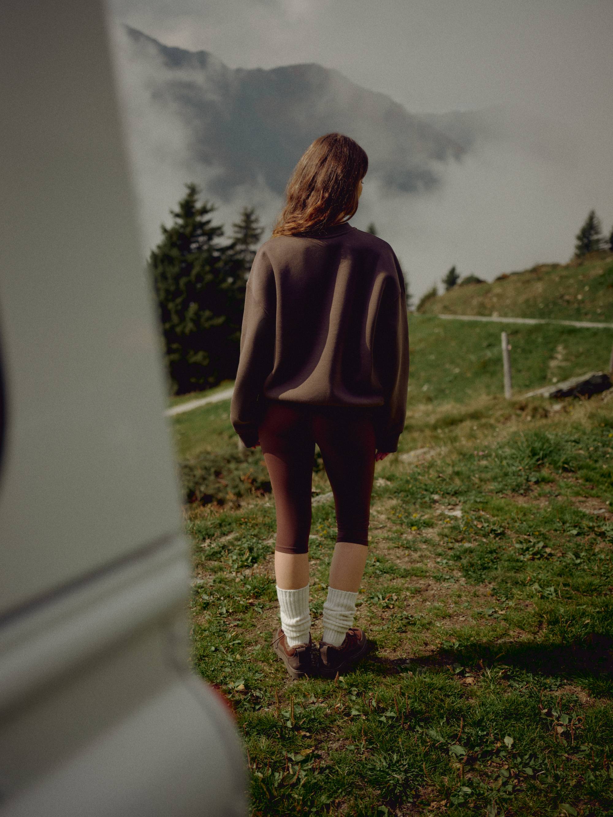 Woman wearing espresso CASPARA Cloudform capri leggings on a mountain hillside.
