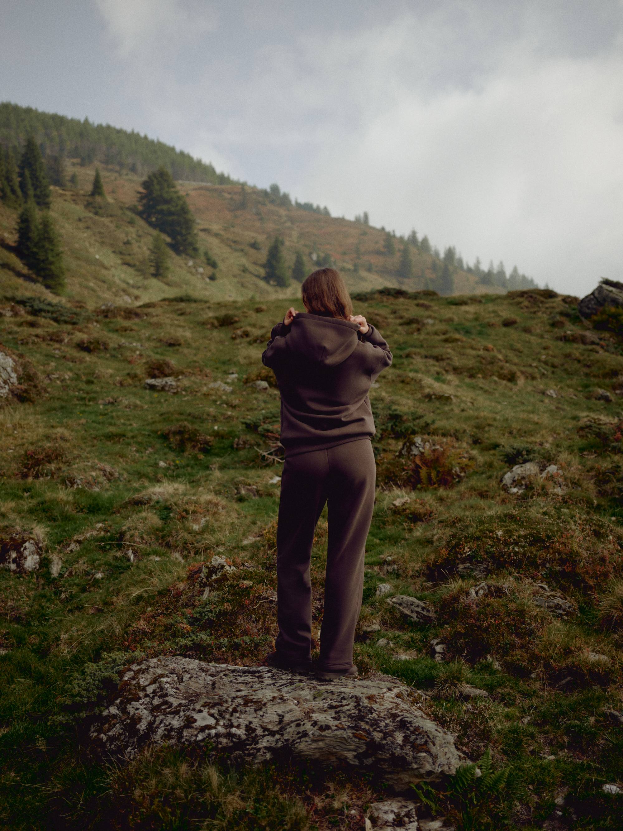 Woman wearing an espresso CASPARA CS sweat set standing on a mountain hillside.