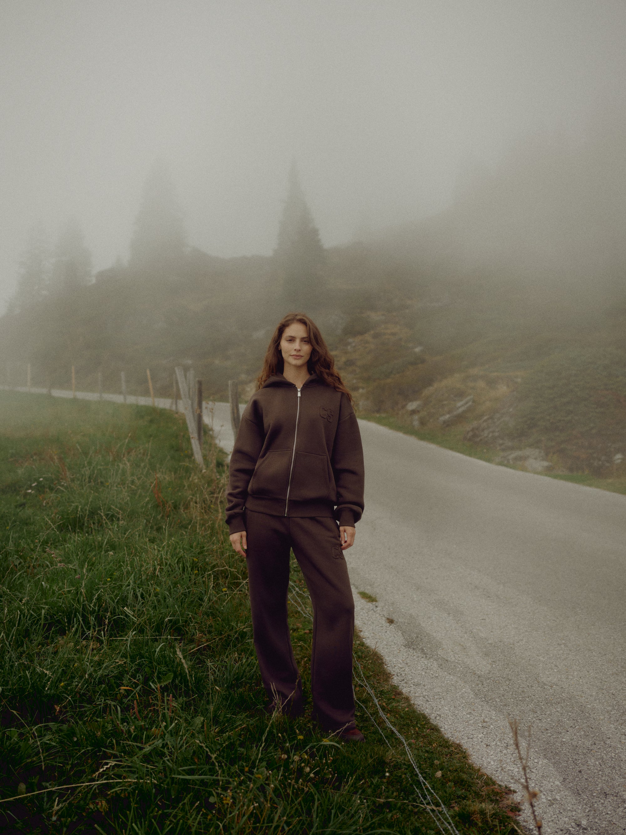 Woman wearing an espresso CASPARA CS zip hoodie on a foggy mountain road.
