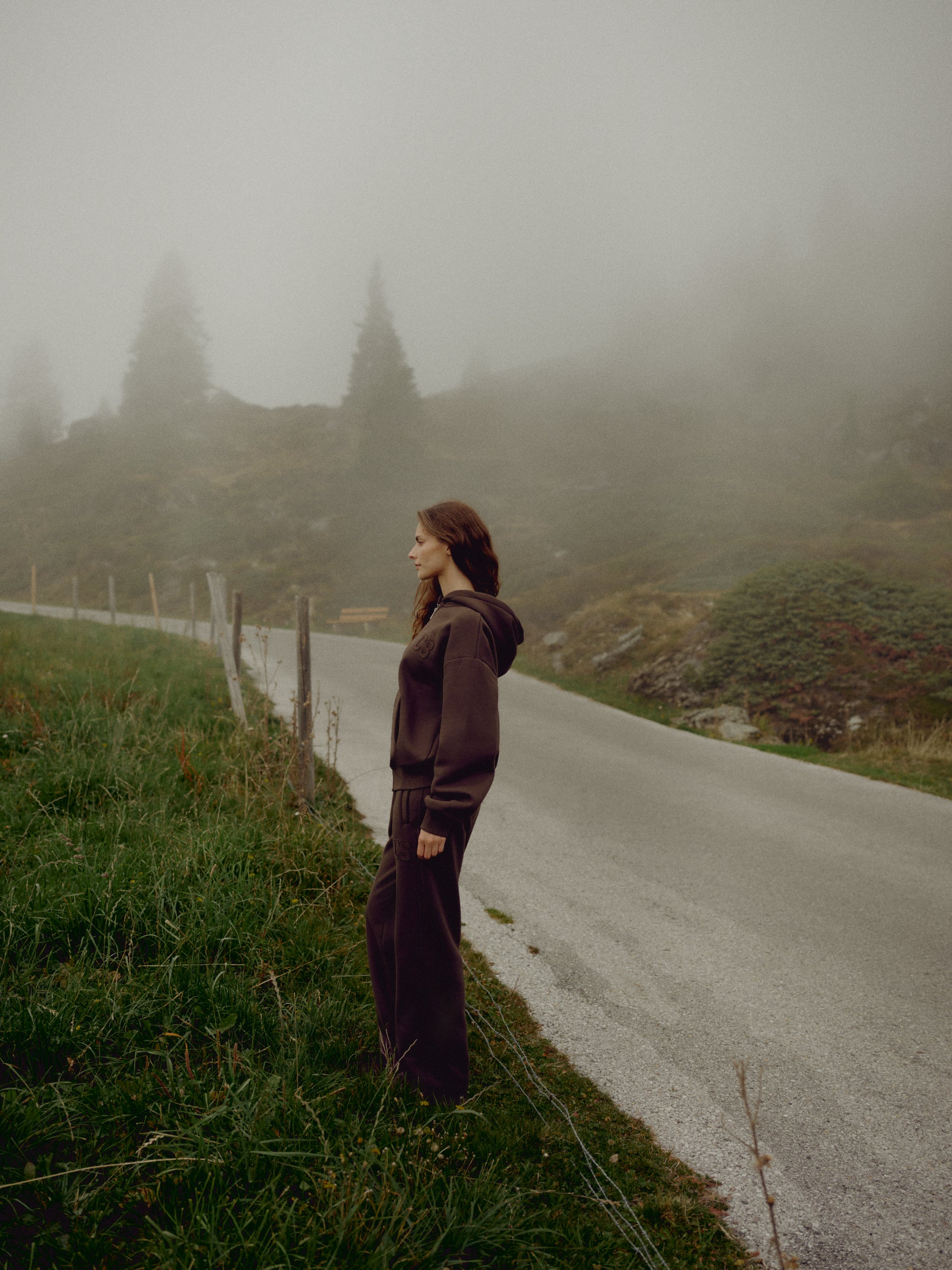 Woman wearing an espresso CASPARA CS zip hoodie standing on a foggy mountain road.