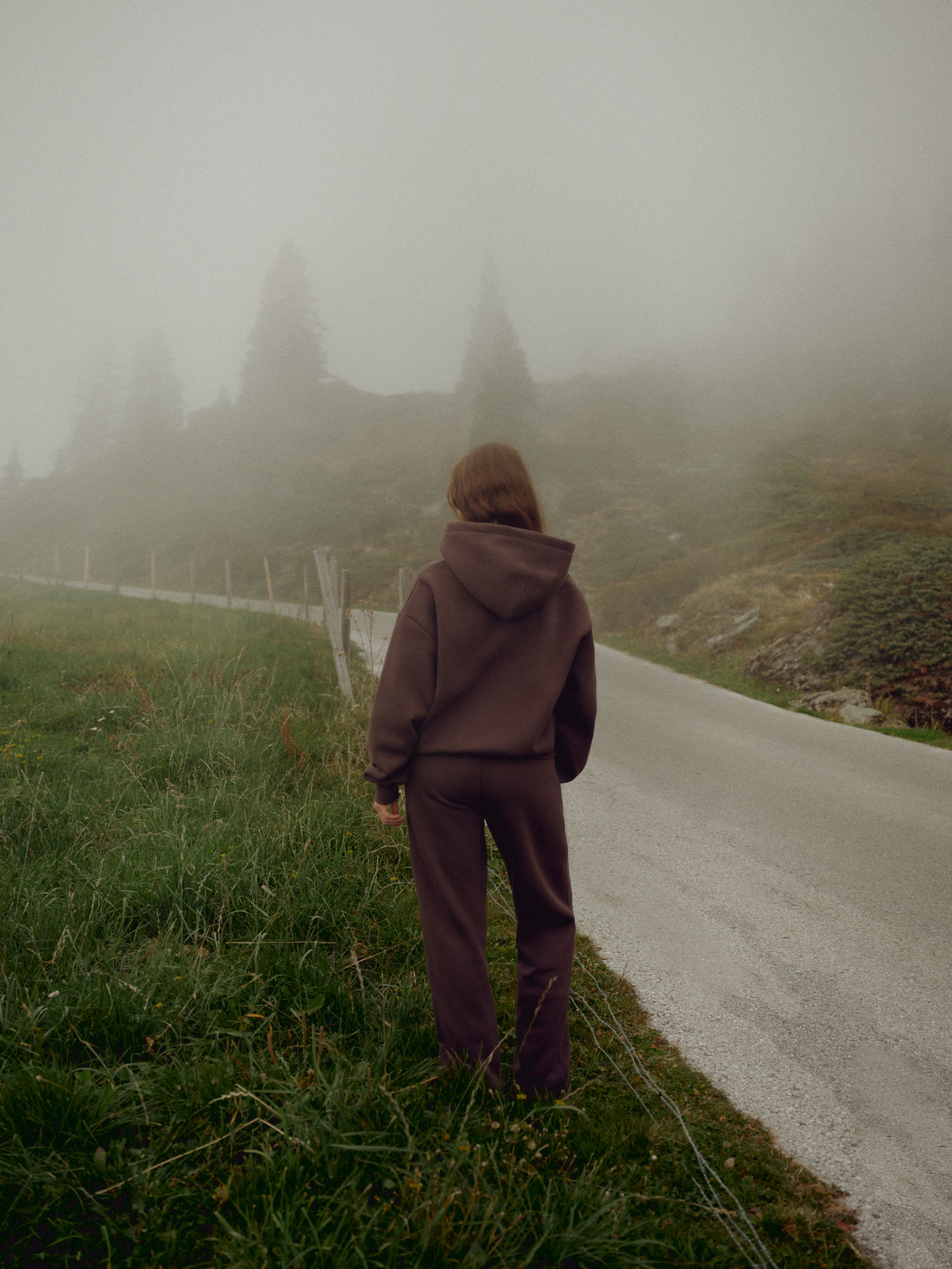 Woman wearing an espresso CASPARA CS zip hoodie standing on a foggy mountain road.
