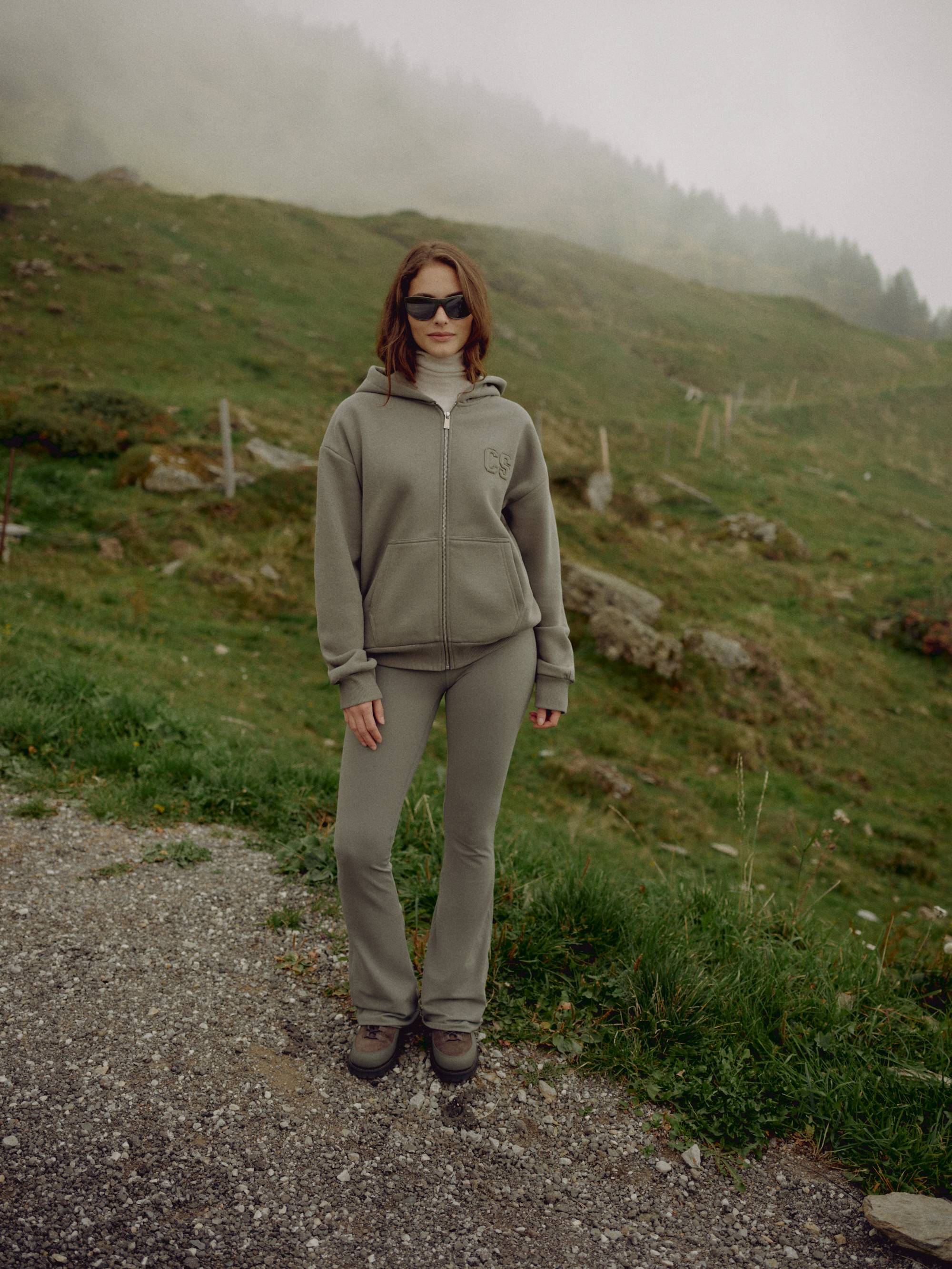 Woman wearing a khaki CASPARA CS zip hoodie standing in a foggy mountain landscape.