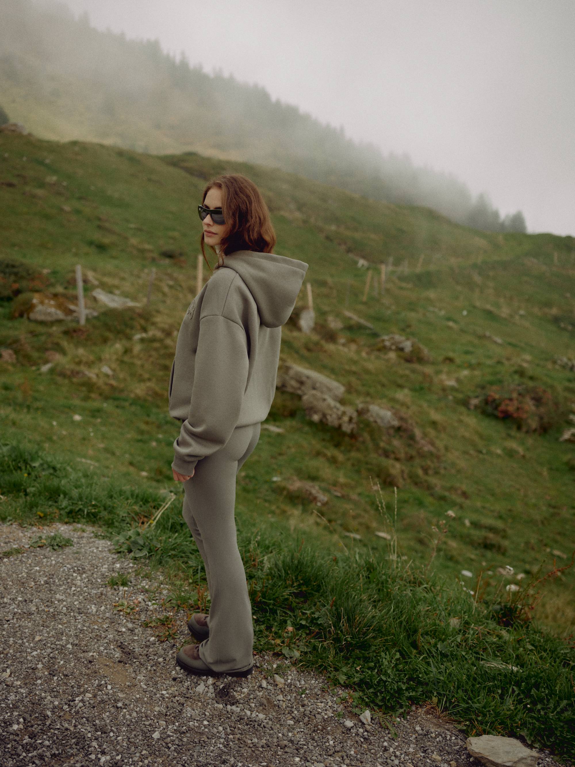 Woman wearing a khaki CASPARA CS zip hoodie standing on a foggy hillside.