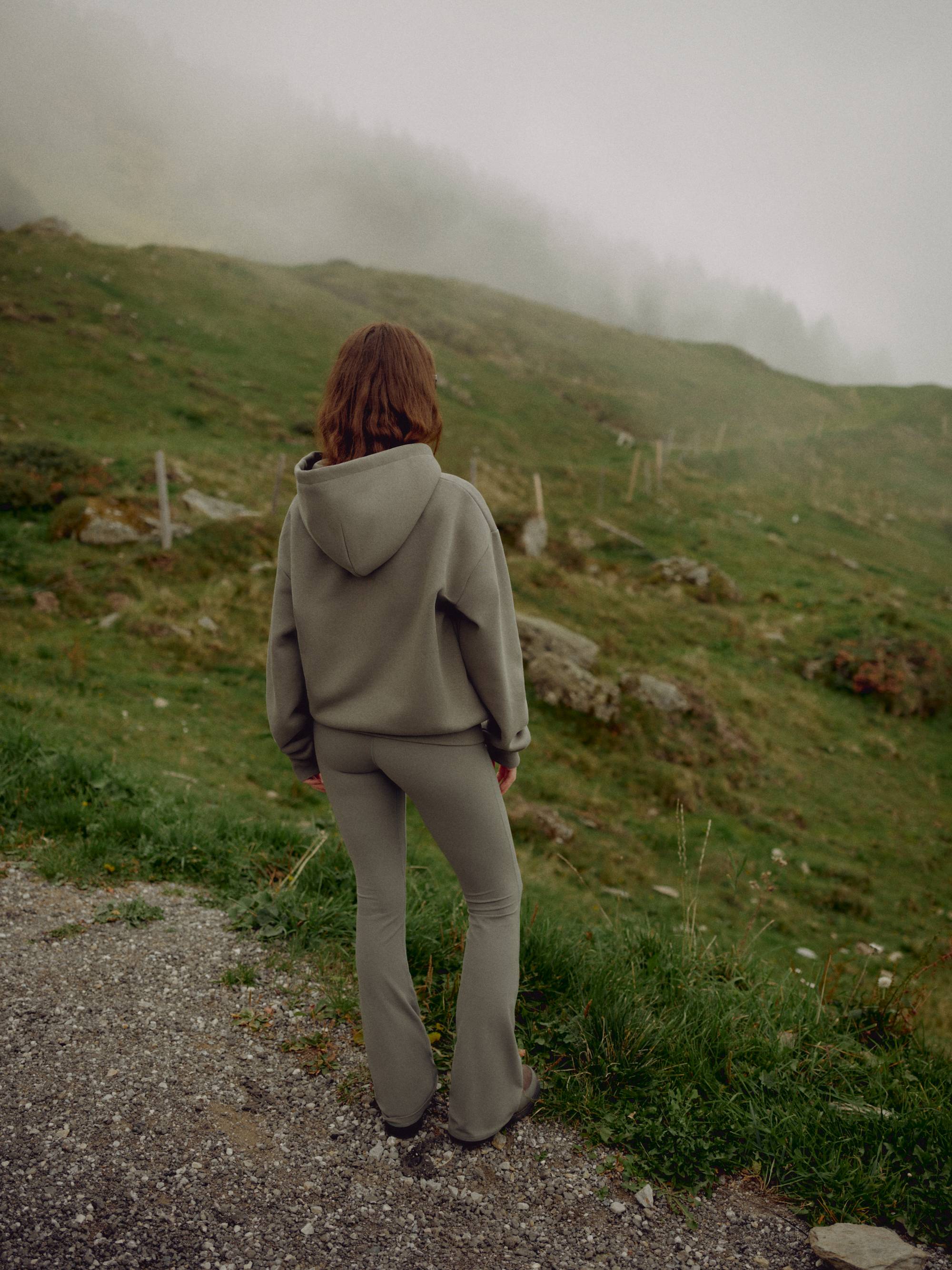 Woman wearing a khaki CASPARA CS zip hoodie standing on a foggy mountain hillside.