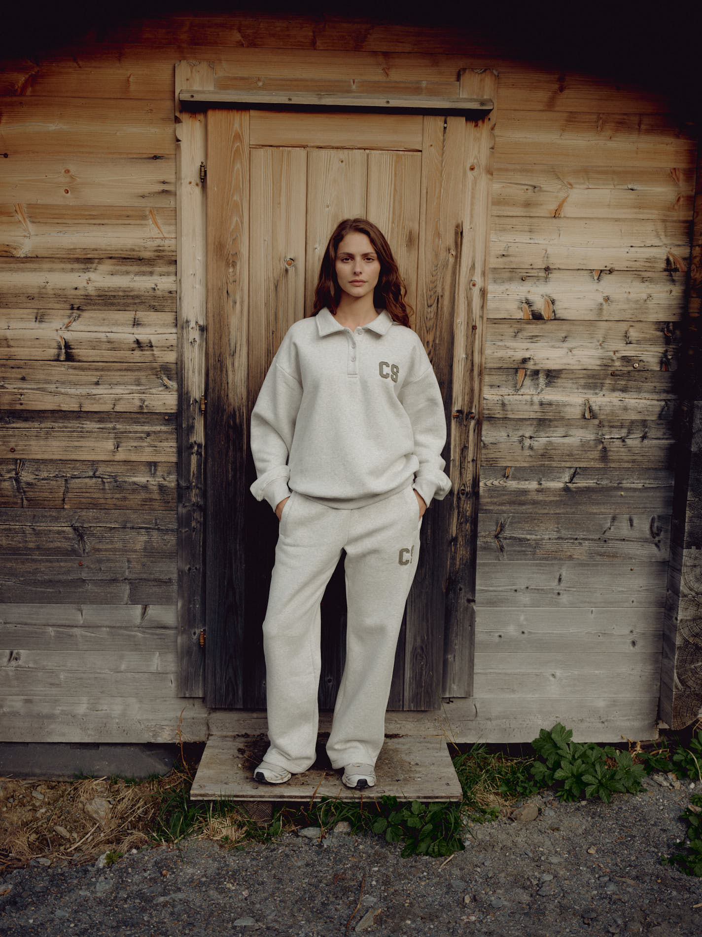 Woman wearing grey melange CASPARA CS sweatpants and polo sweater outside a wooden cabin.