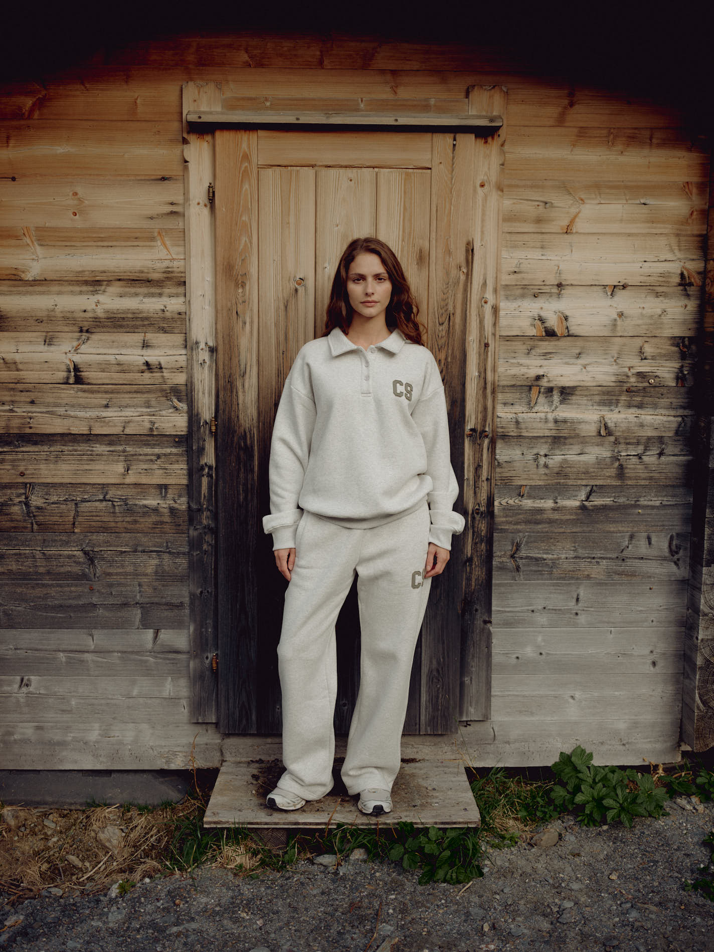 Woman wearing grey melange CASPARA CS sweatpants and a matching sweatshirt by a wooden cabin.