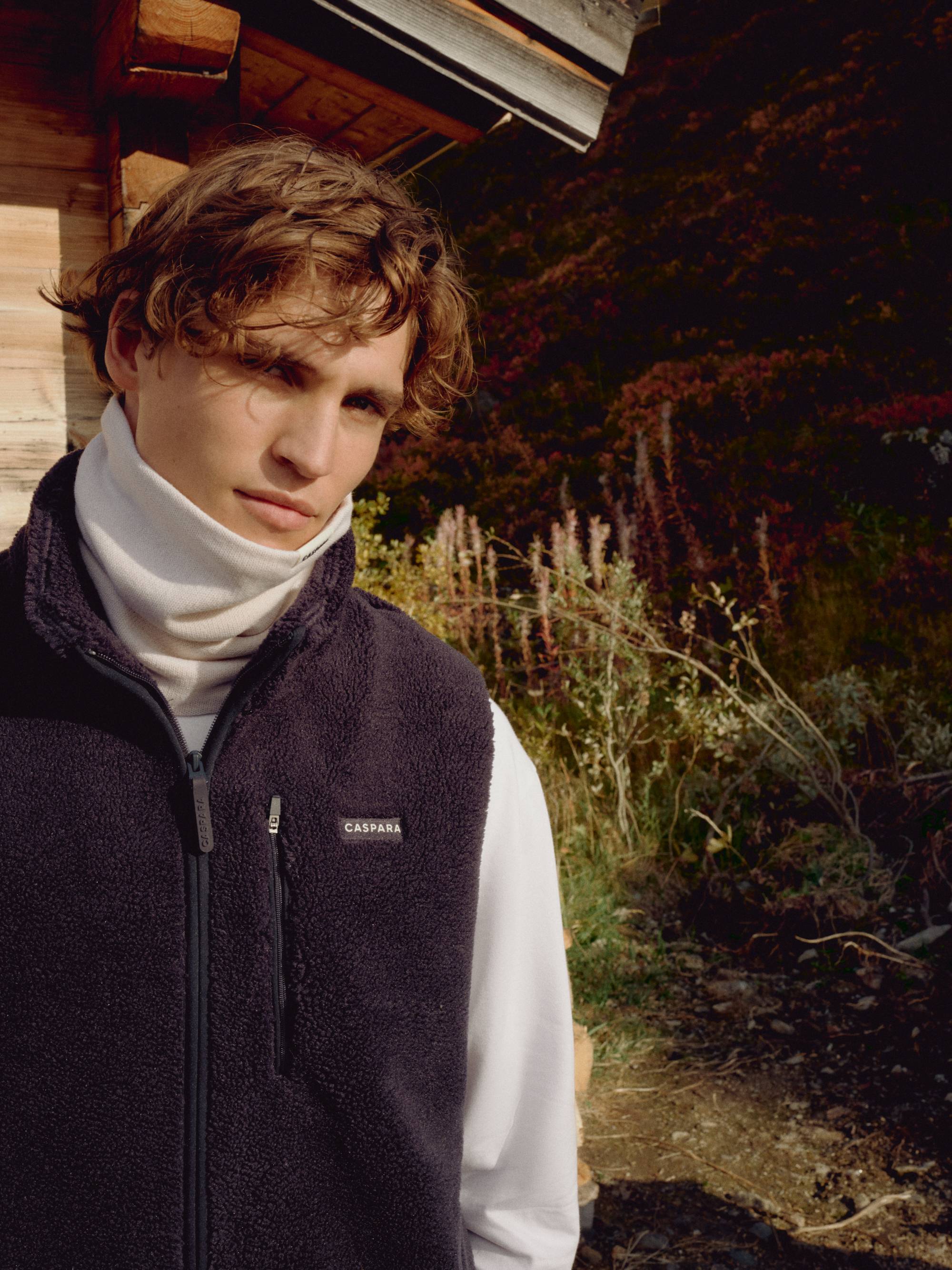 Man wearing a creme CASPARA Classic Neckwarmer and fleece vest outdoors.