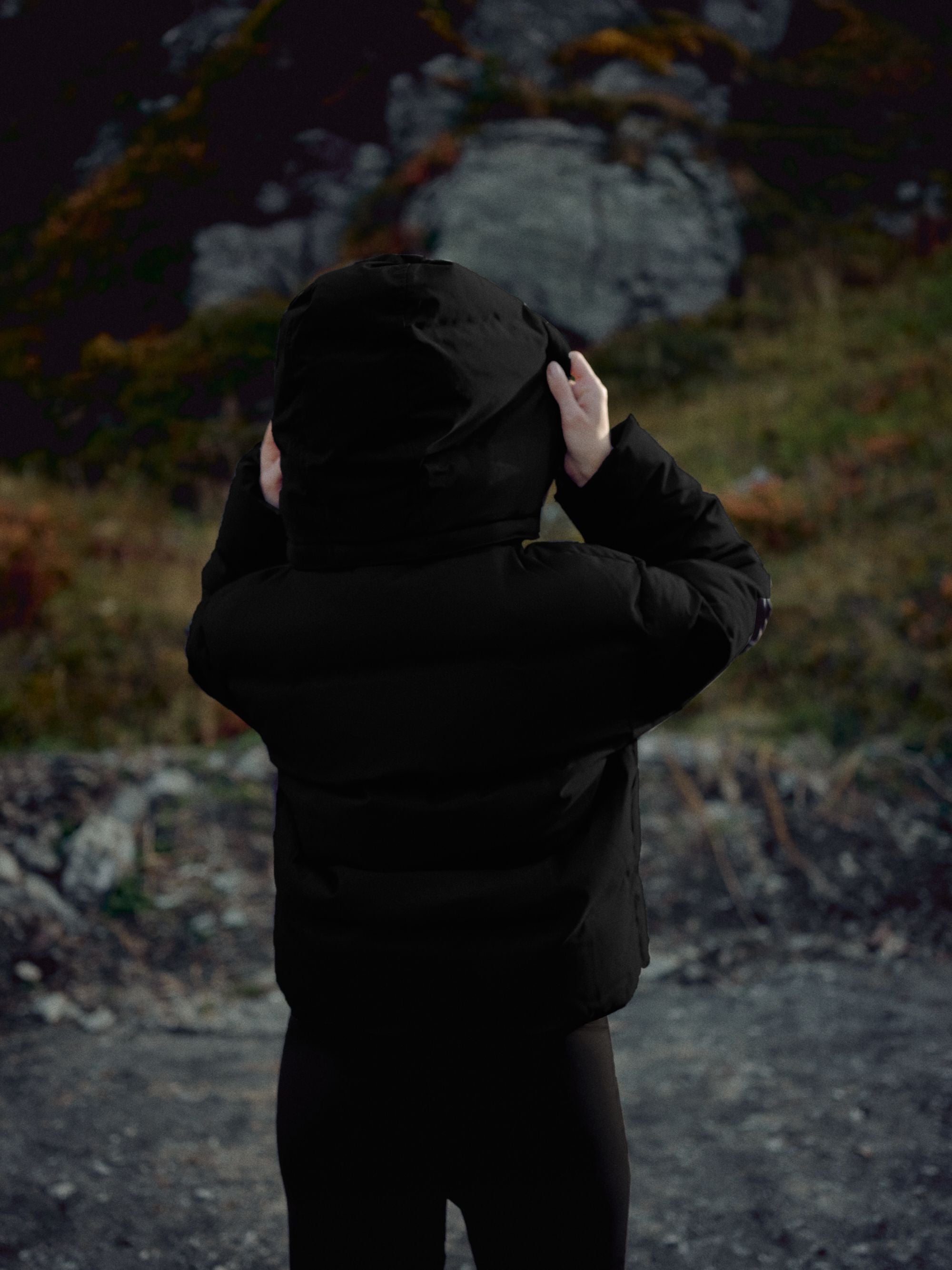 Back view of a woman wearing a black CASPARA Aurora puffer jacket with the hood up outdoors.